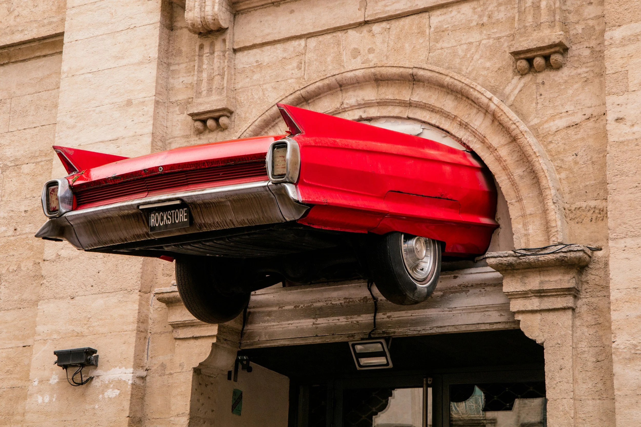 Une sculpture de voiture rouge, suspendue au-dessus d'une porte d'entrée, dans un style rétro et artistique.