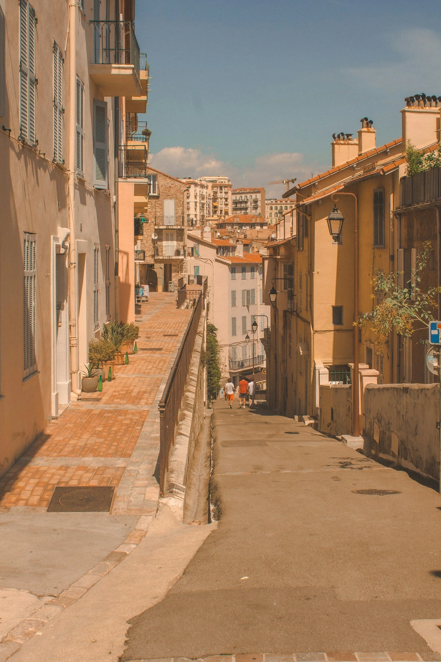 Vue d'une rue en pente dans une ville avec des bâtiments colorés, des lampadaires et un ciel ensoleillé