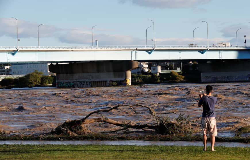 A man takes a picture of the Tama river, which reached flood risk level Saturday night. | REUTERS