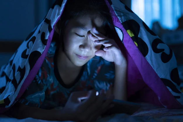 Girl using mobile phone on dark bed in the bedroom, eye strain t