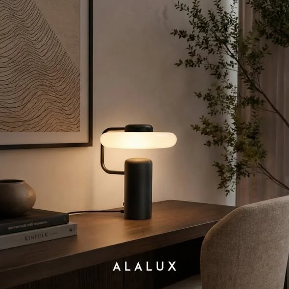  Em uma composição de interiores, a luminária de mesa VOREN demonstra sua capacidade de transformar a atmosfera de um espaço por meio da combinação entre iluminação e design. Posicionada sobre um móvel de madeira, a peça estabelece um ponto focal ele