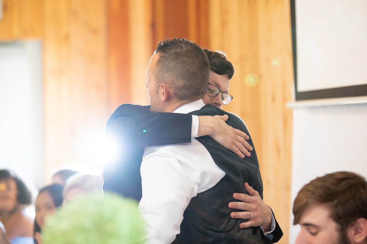 Groom and groomsman hugging during toasts at wedding reception. 