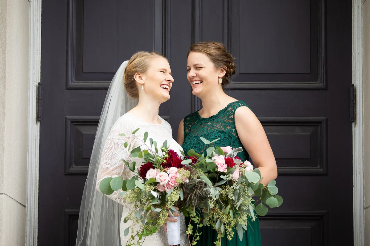 Bride and matron of honor laughing during formal photos.