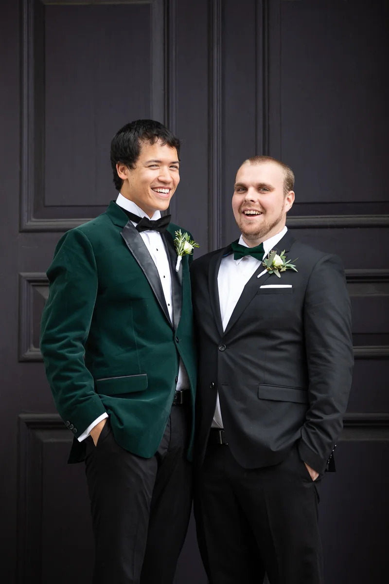 Groom and groomsman laughing during formal photos.