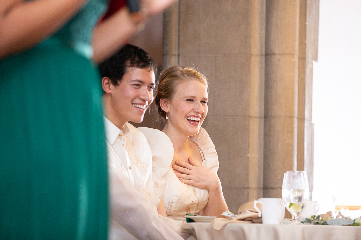 Bride and groom laughing during wedding toasts at reception.