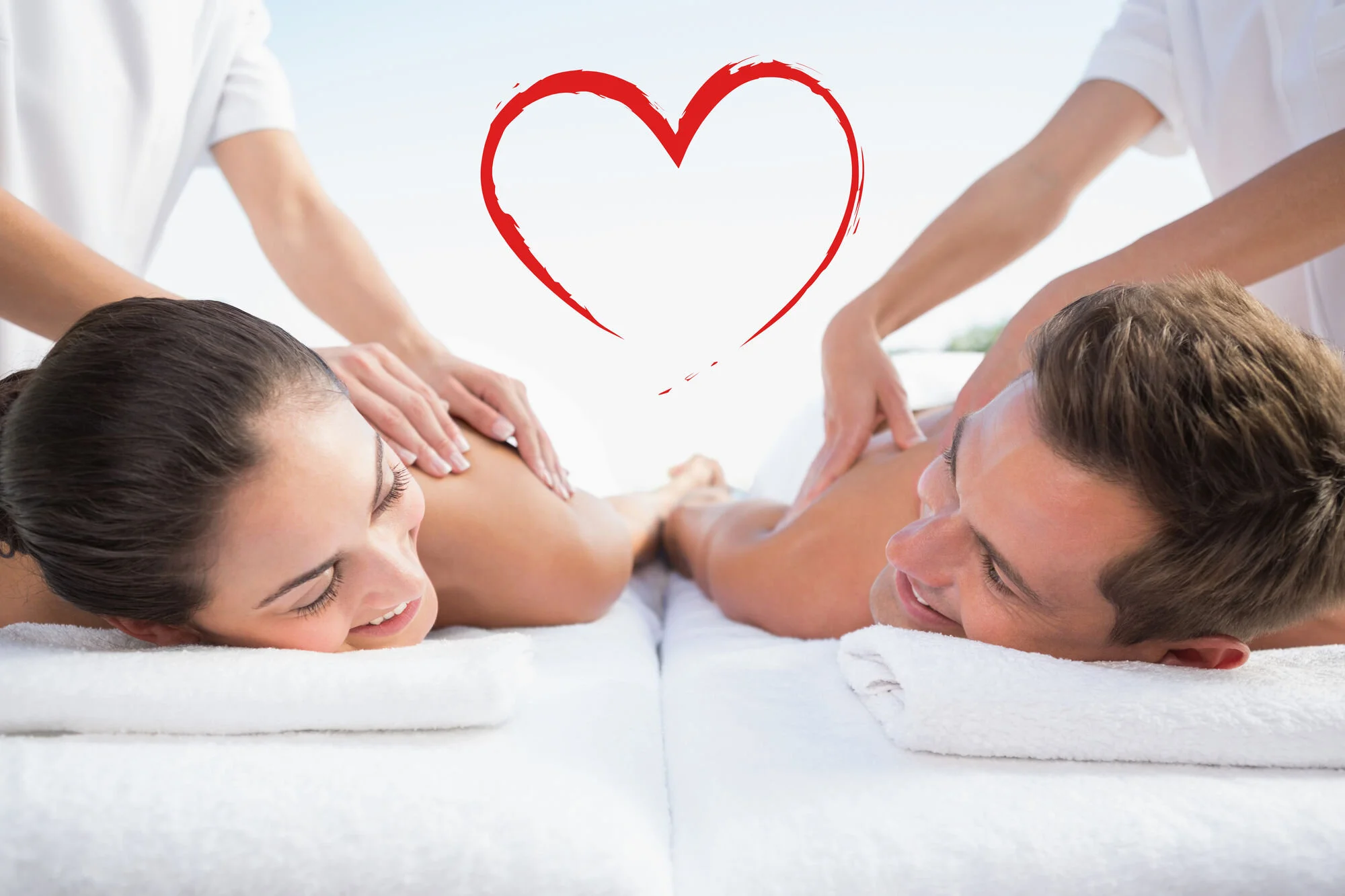 A woman and a man receiving massages from two massage therapists in an outdoor setting with a stylized red heart graphic above them.