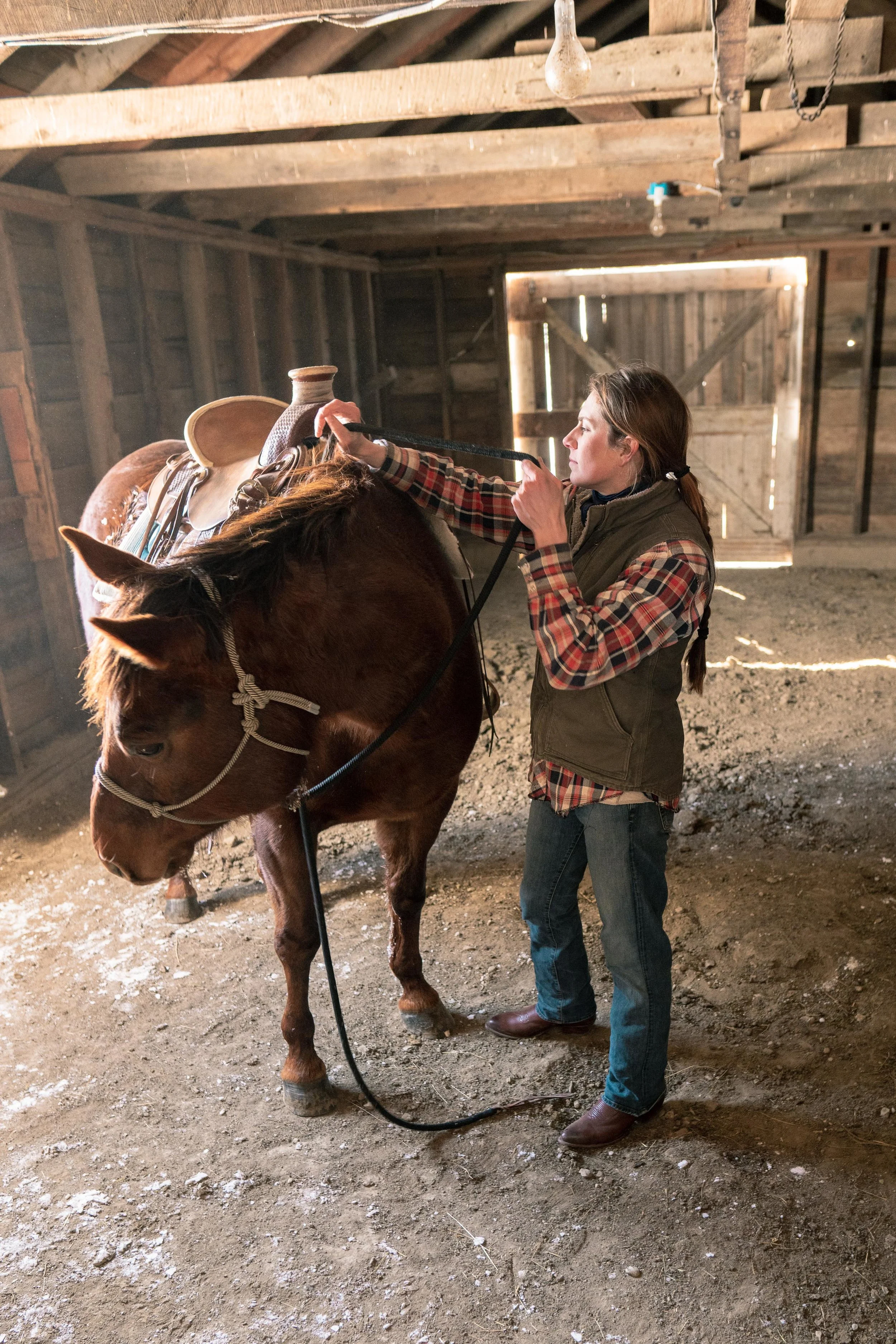 Jenna Flatgard wearing Tecovas while working her horse in her barn in eastern Montana.