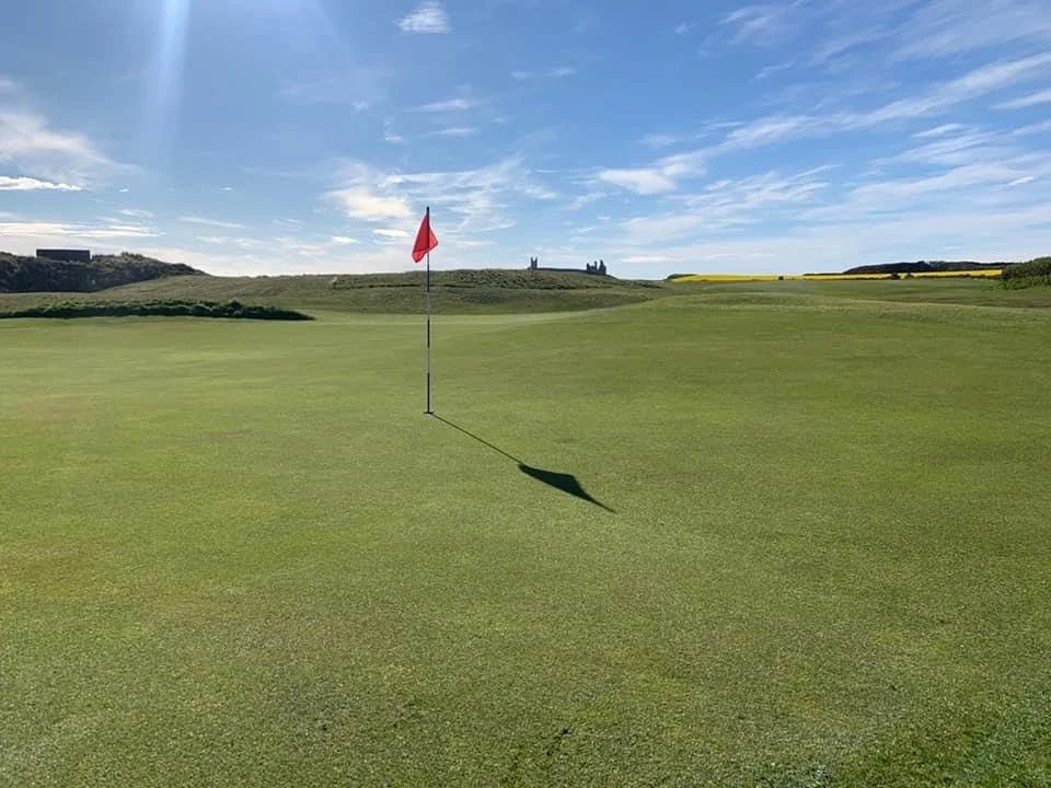 A green at Dunstanburgh with the castle on the horizon