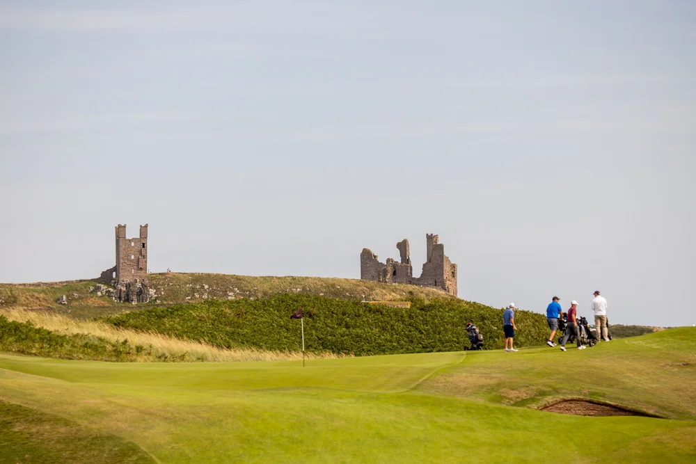Golfers walking beneath the ruins of Dunstanburgh Castle