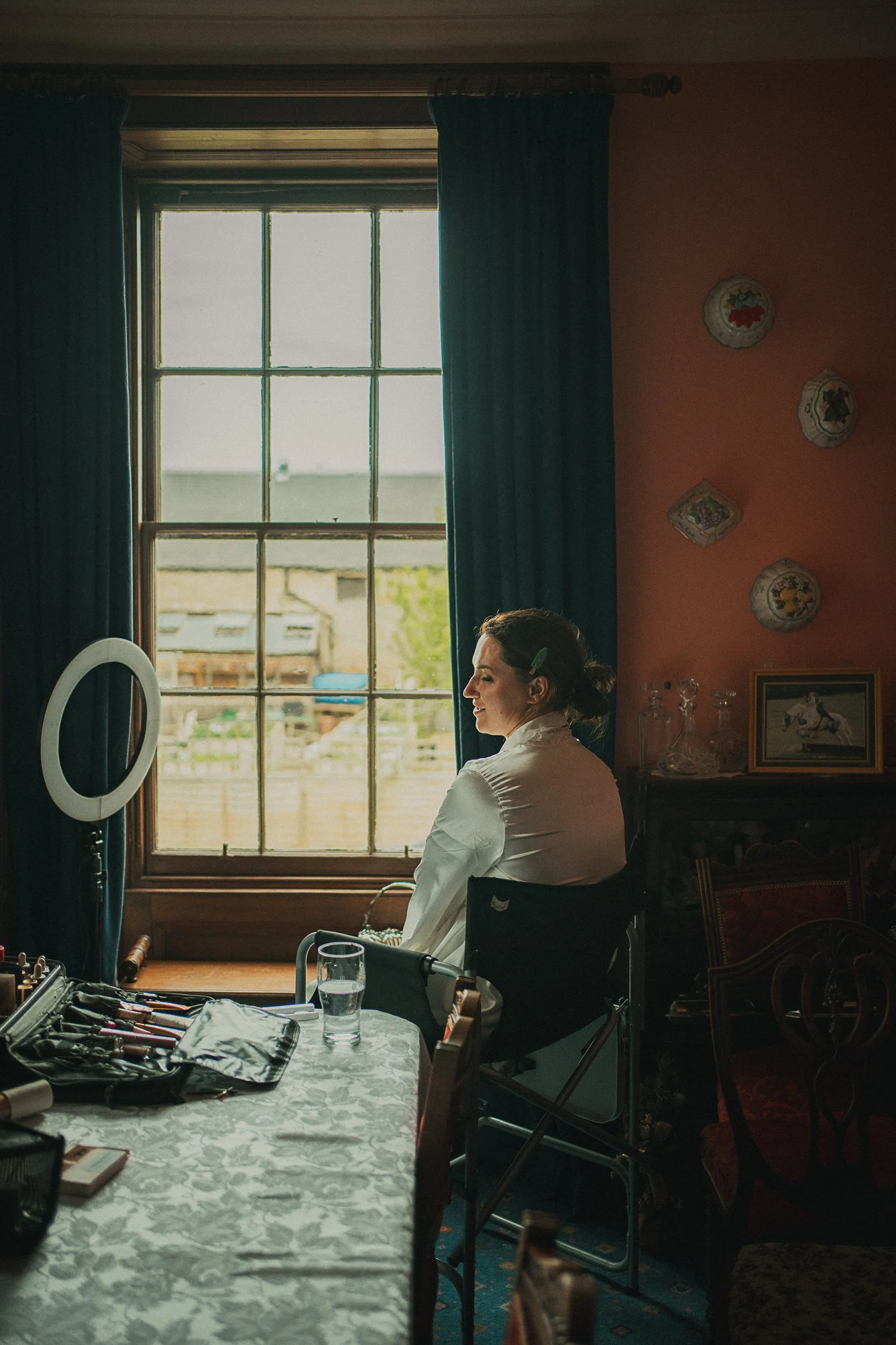 Bride Libby during morning preparations, sitting by the window while makeup is applied before her Scottish Borders wedding.