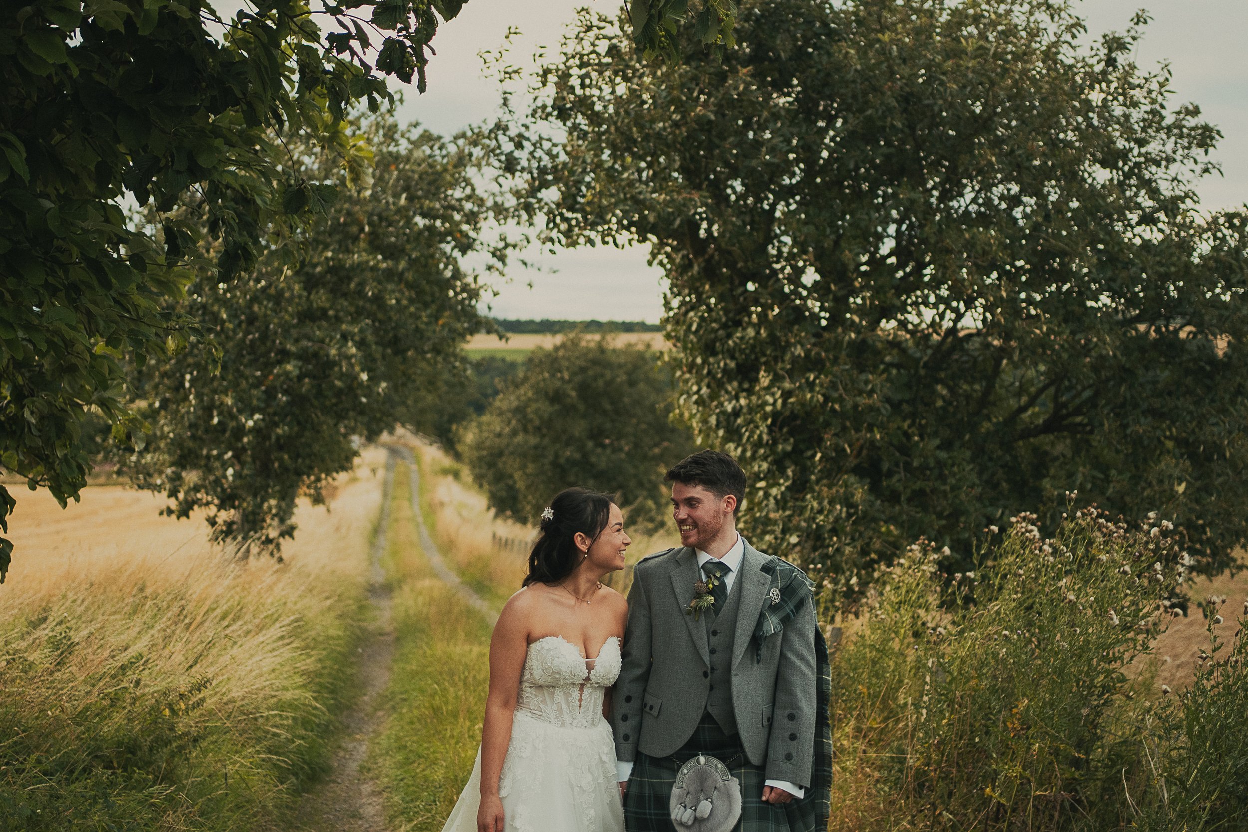 Josie and David walking together along a country farm lane during their wedding at Rossie on the Earn