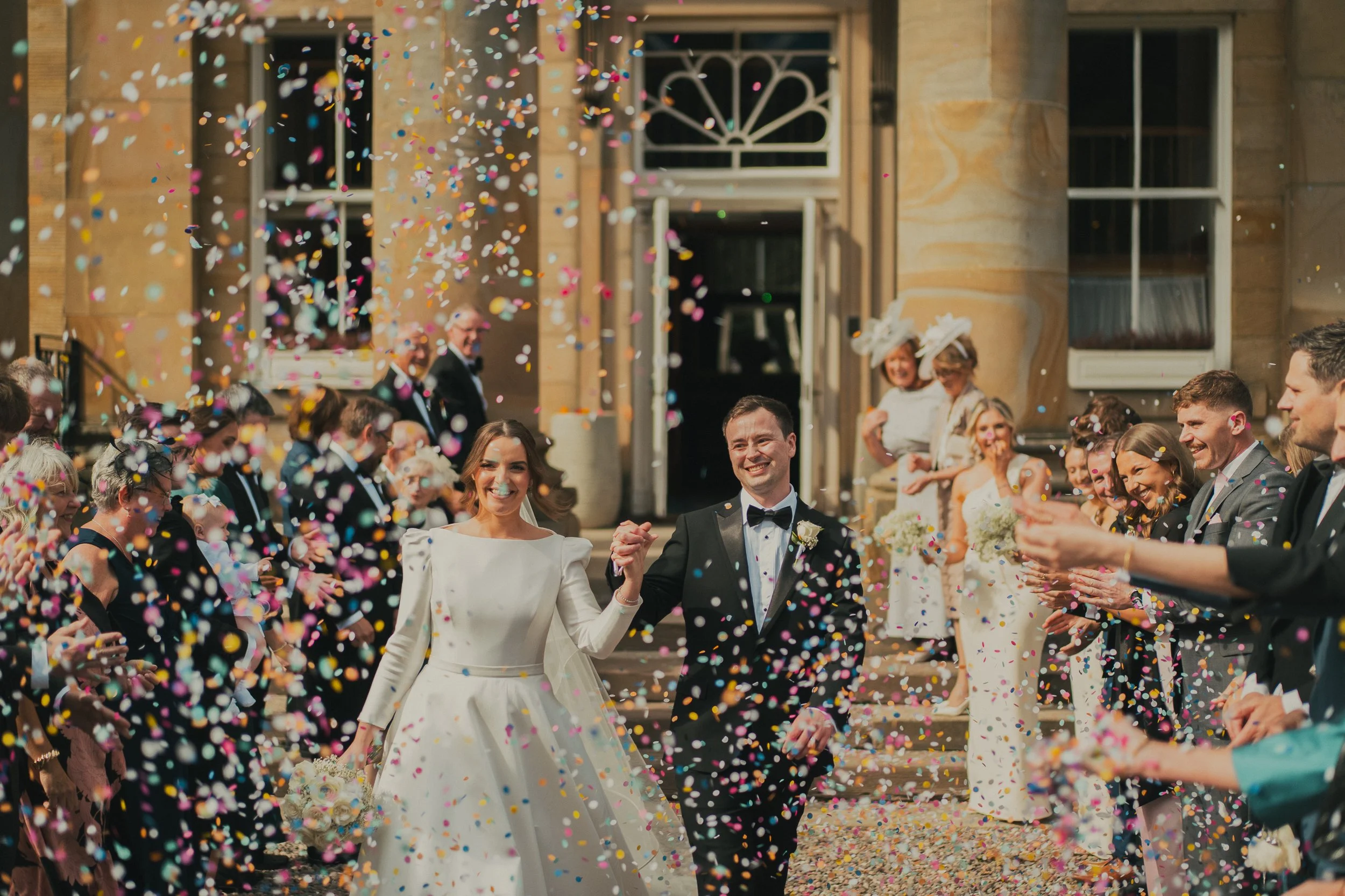 Alyssa and Ian walking through a colourful confetti tunnel after their wedding ceremony at Balbirnie House