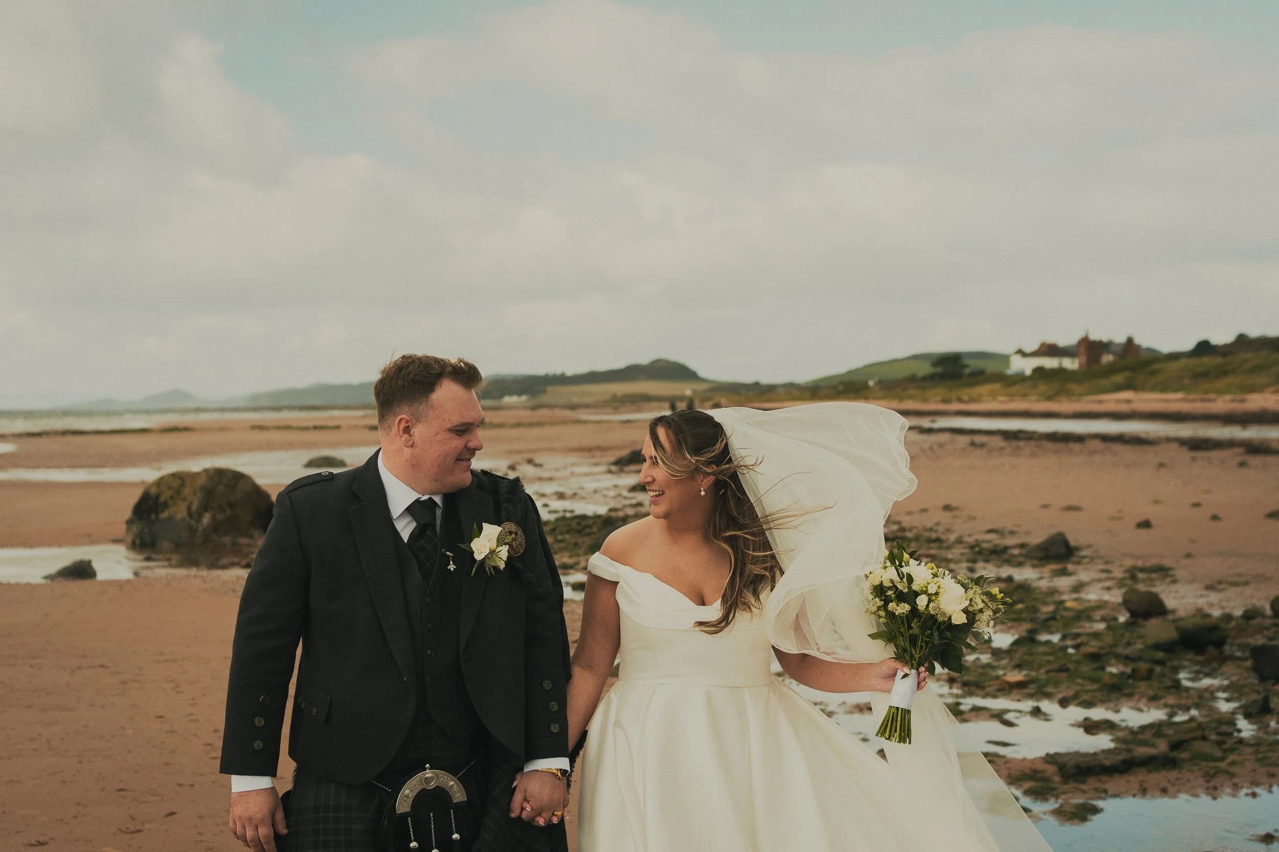 Gill and Callum smiling at each other while holding hands on the beach at Seamill Hydro