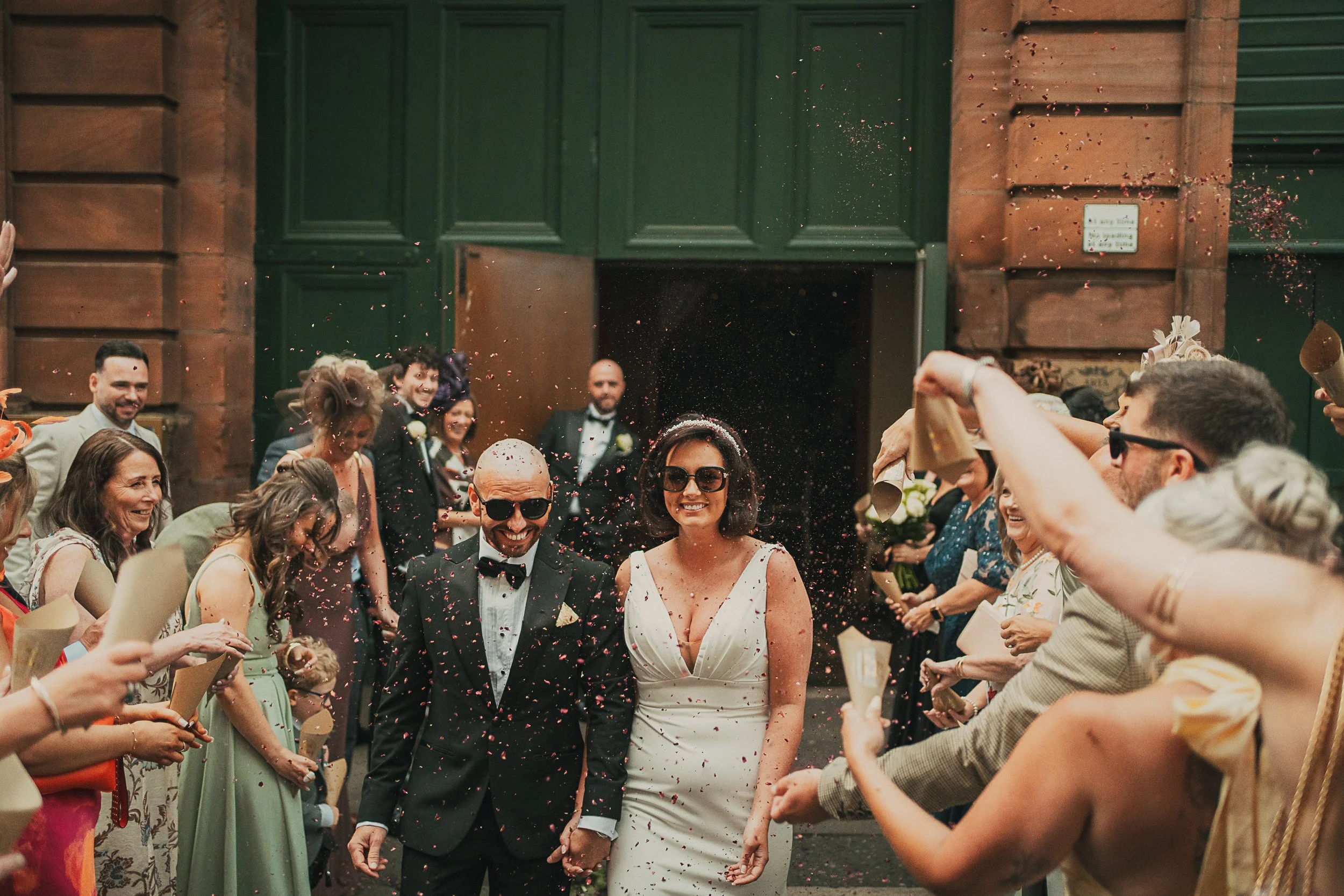 Lynsey and Paul walk through confetti wearing sunglasses outside Arta Glasgow after their Merchant City wedding ceremony.