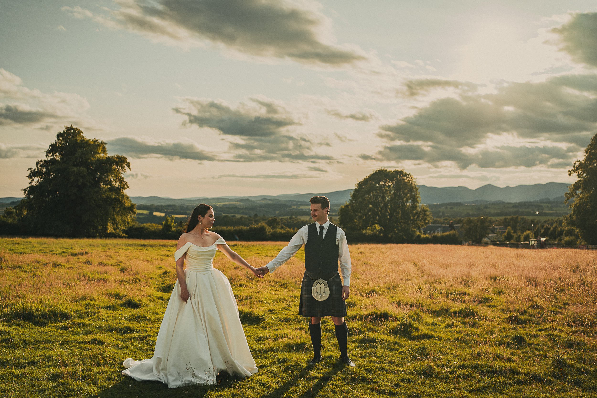 Claire and Adam holding hands in a field during golden hour at their Killearn wedding
