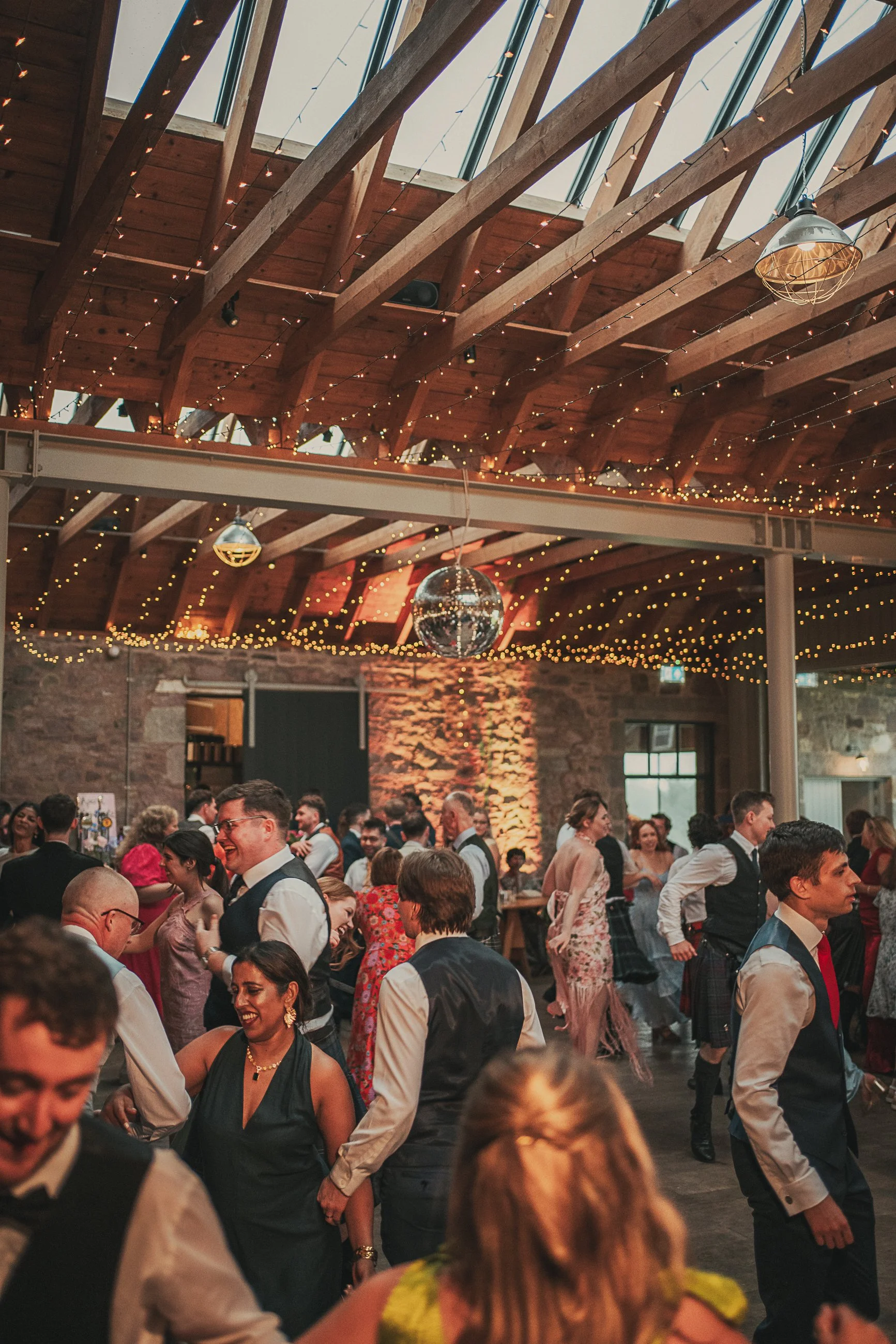 Guests celebrating on the lively dance floor beneath fairy lights and disco balls at Guardswell Farm wedding.
