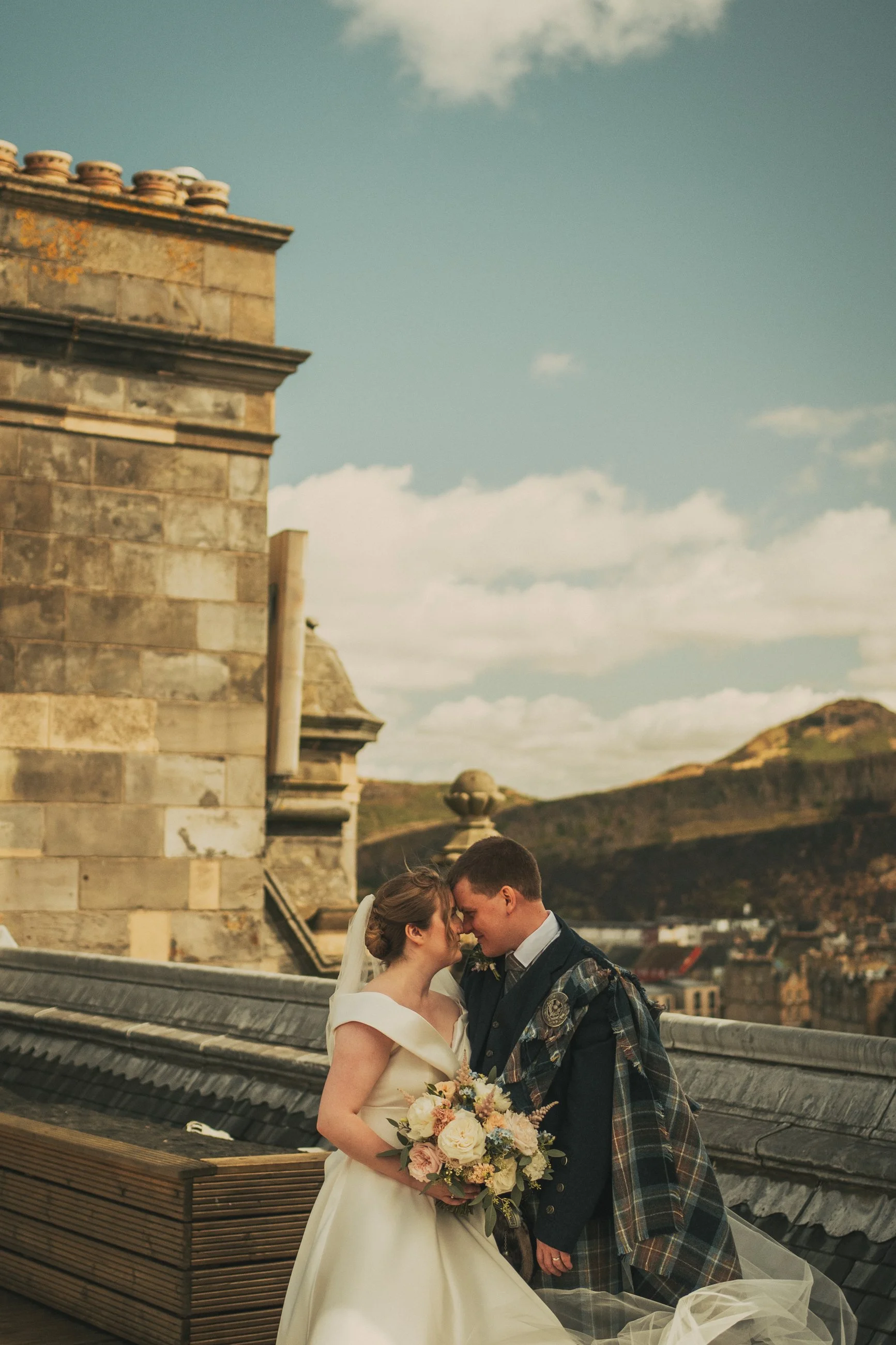 Alexandra and Gavin embracing on the rooftop of The Balmoral Hotel overlooking Edinburgh