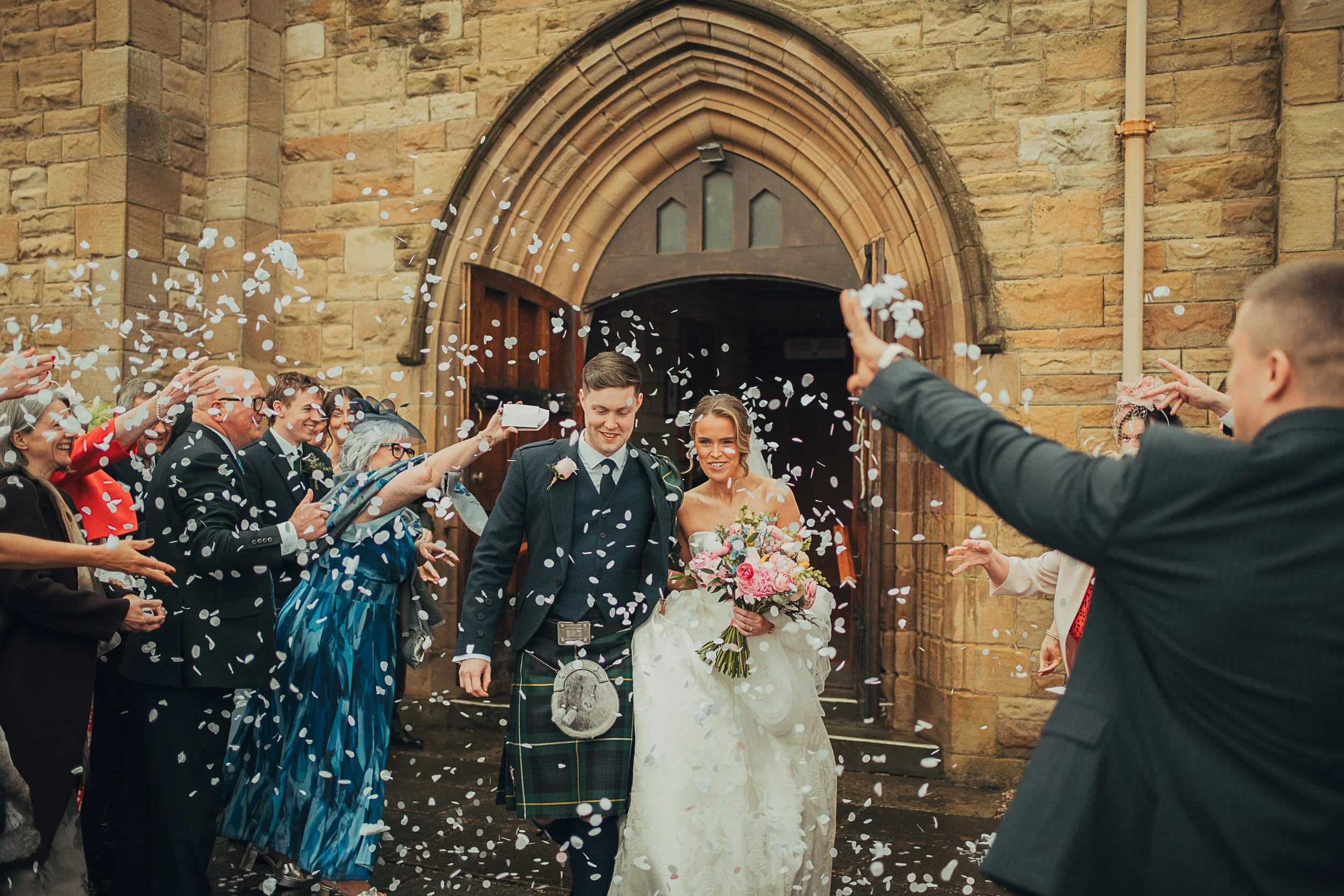 Bride and groom walking through confetti outside Portland Church of Scotland in Troon after their wedding ceremony..
