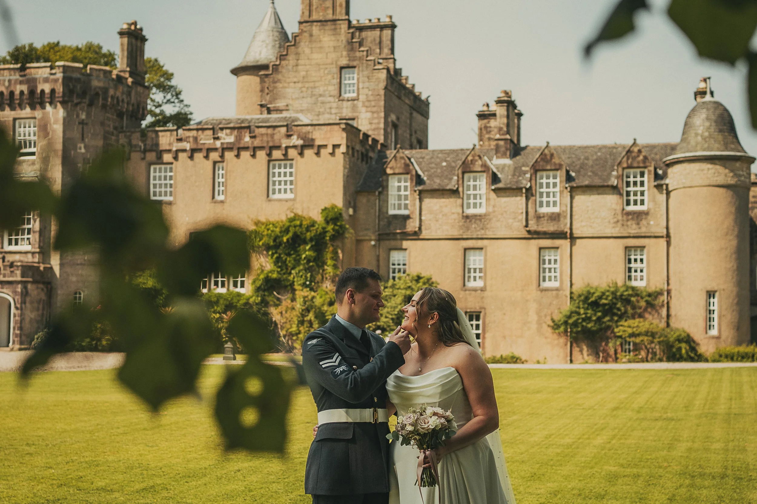 Bride and groom looking at each other in front of Boturich Castle during their summer wedding on Loch Lomond