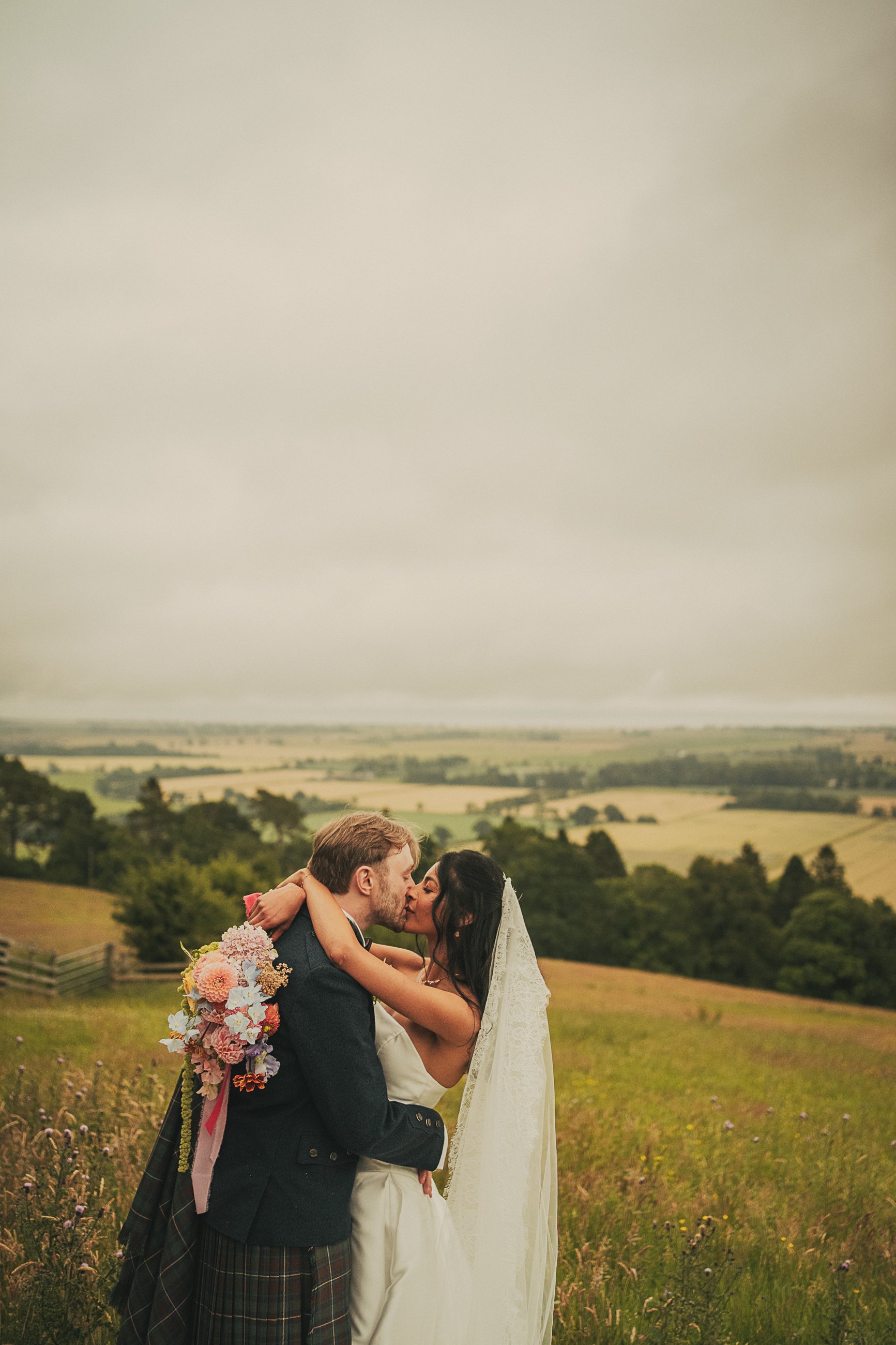Bride and groom sharing a kiss in the countryside during their Guardswell Farm wedding in Perthshire.