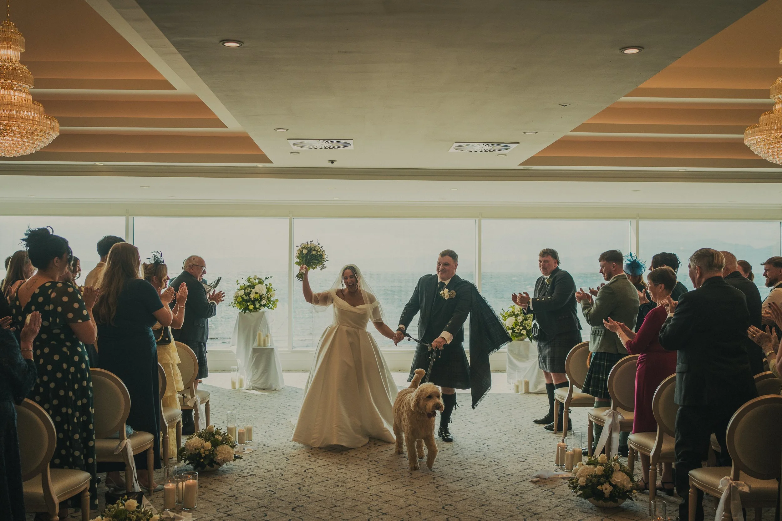 Gill and Callum walking down the aisle with their dog Beamer at their Seamill Hydro wedding ceremony