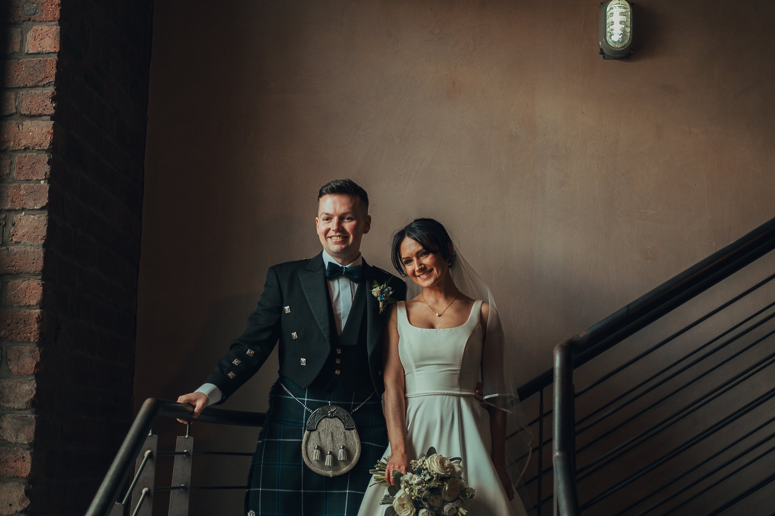Beth and Craig smiling together on the stairs at The Engine Works Glasgow wedding venue