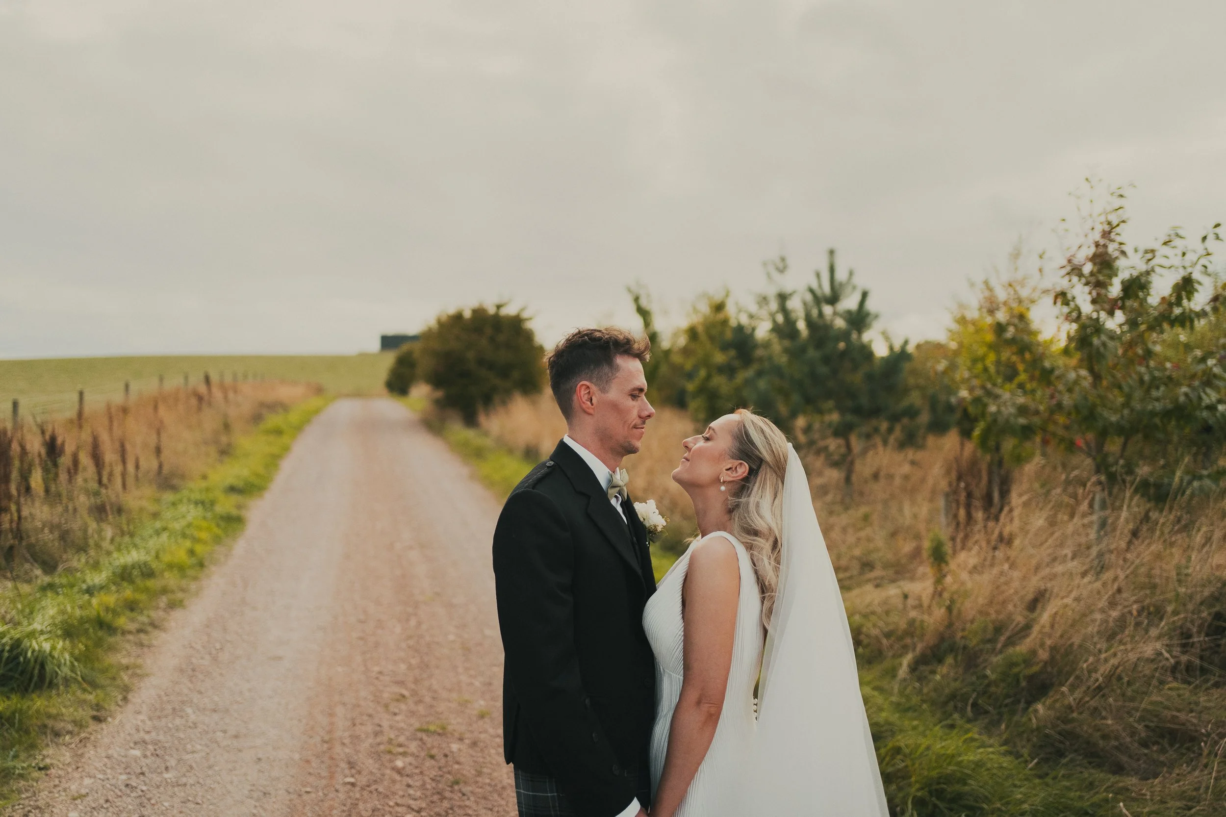 Robyn and Robbie looking into each other's eyes on the farm road at their Falside Mill wedding in Fife