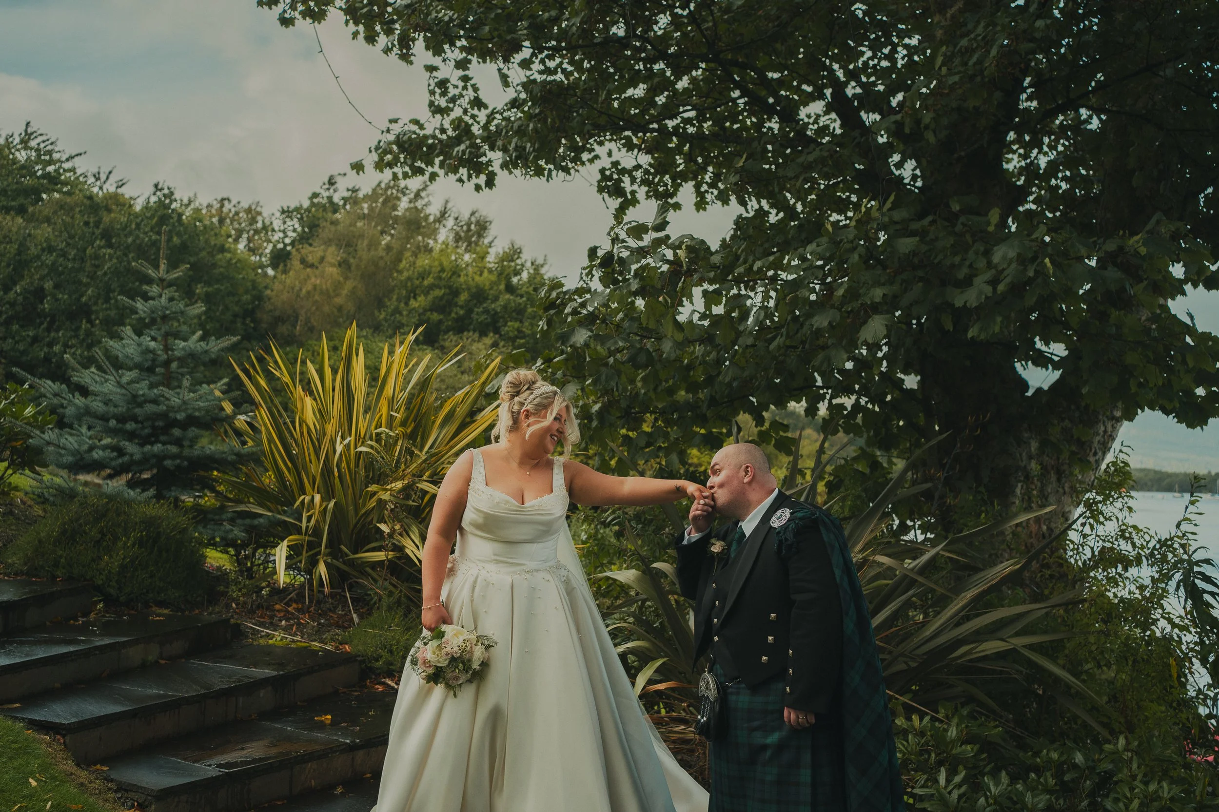 Nicky kissing Laura's hand in the gardens at The Cruin during their Loch Lomond wedding