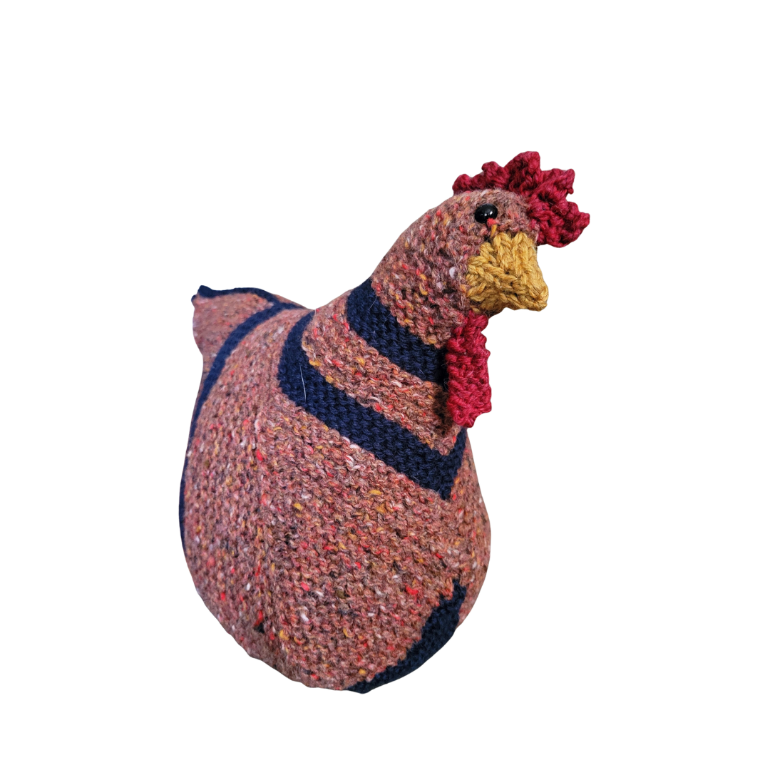 A handmade knitted chicken plush with a pink, blue, and yellow knitted coat and details, set against a white background.