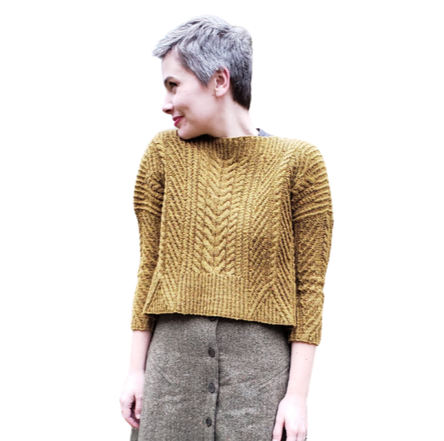 Woman with short gray hair wearing a mustard yellow knitted sweater and gray skirt, standing against a white background.