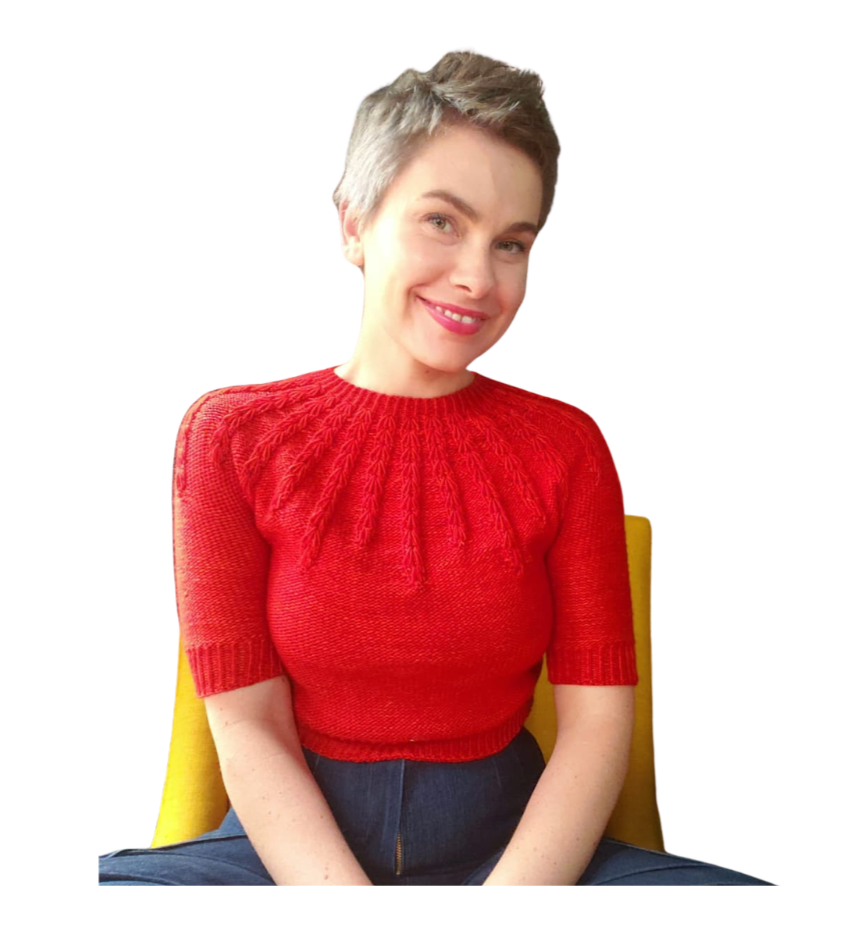A woman with short gray hair smiling, wearing a red sweater with textured patterns, sitting on a yellow chair against a white background.