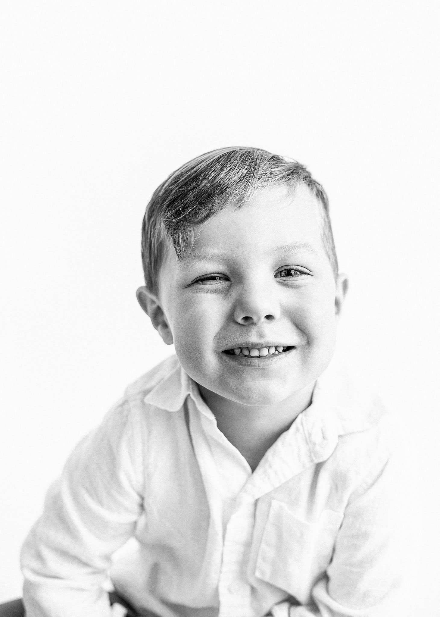 Black and white photo of a smiling young boy in a white shirt.