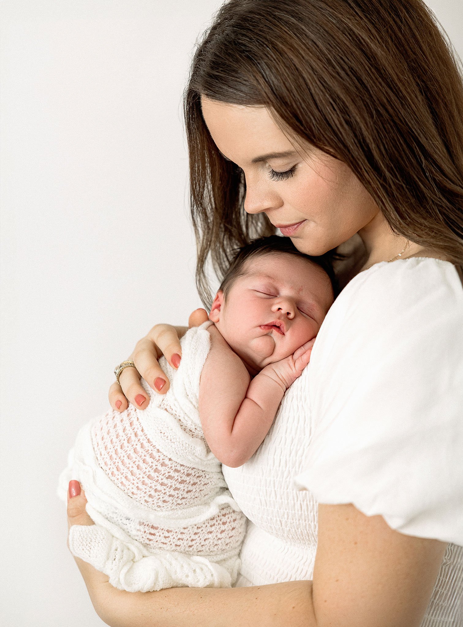 Woman holding sleeping newborn wrapped in a white blanket.