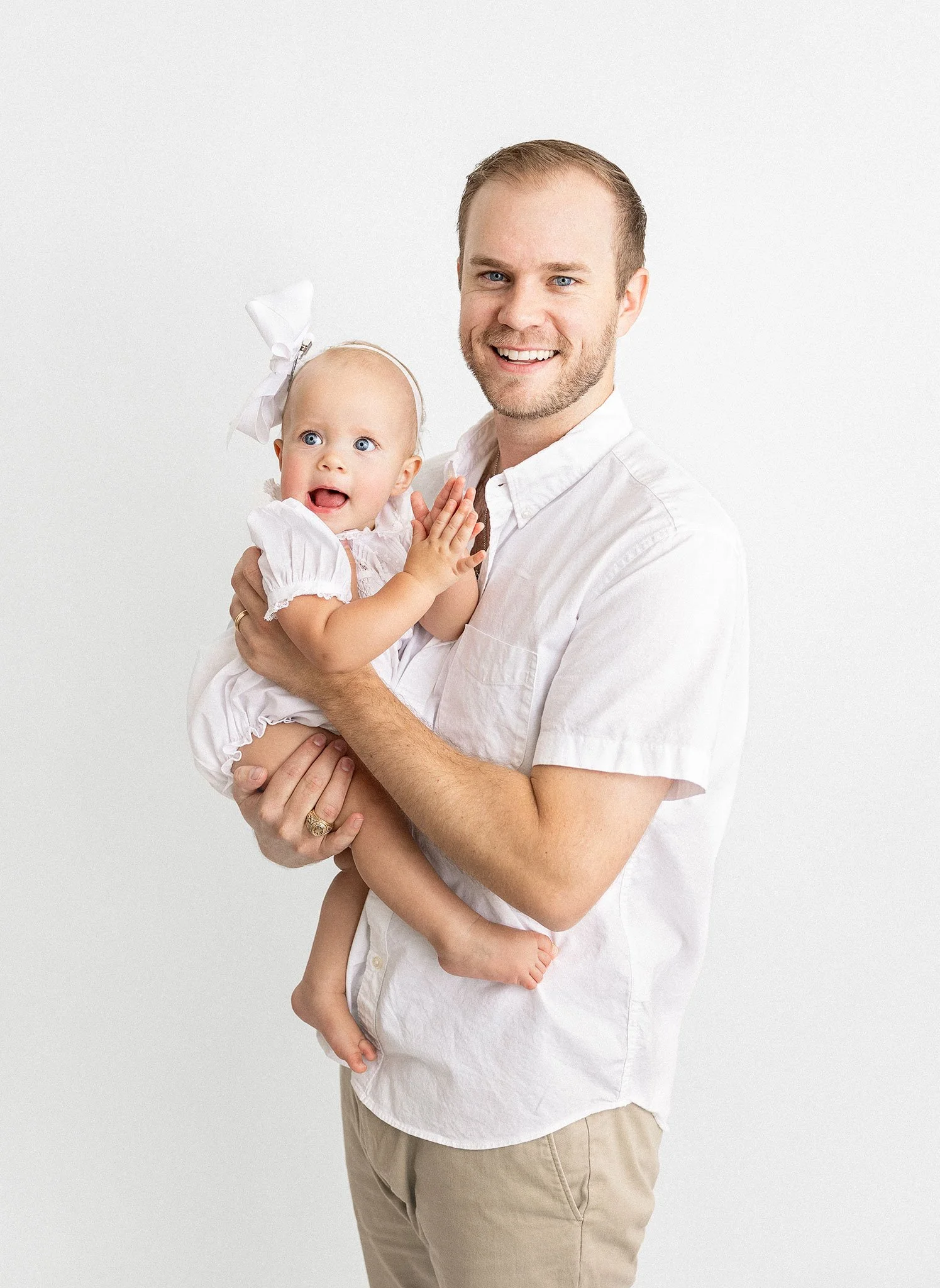 Man holding a baby, both wearing white outfits, against a white background.