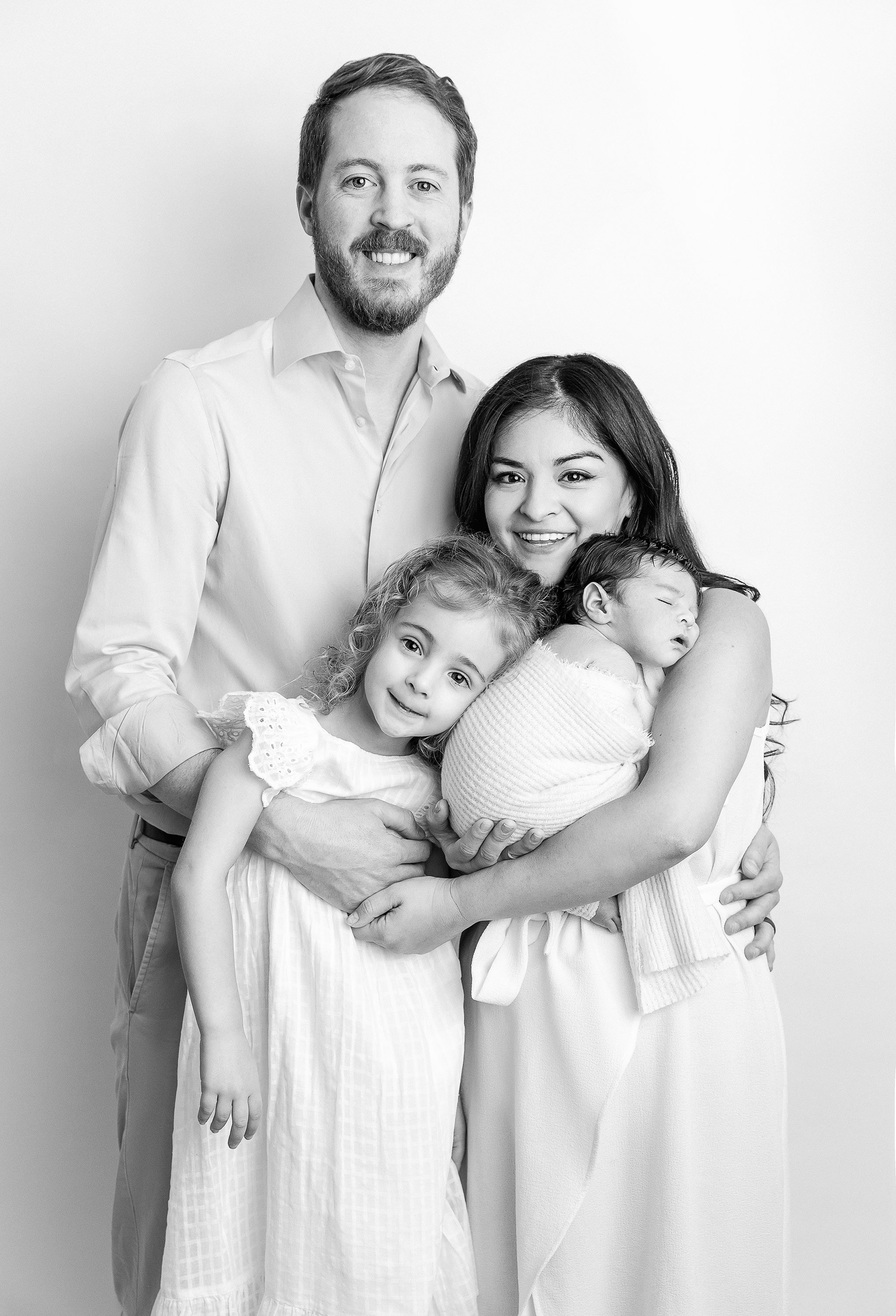 Black and white portrait of a family of five, smiling and hugging, with a plain background.