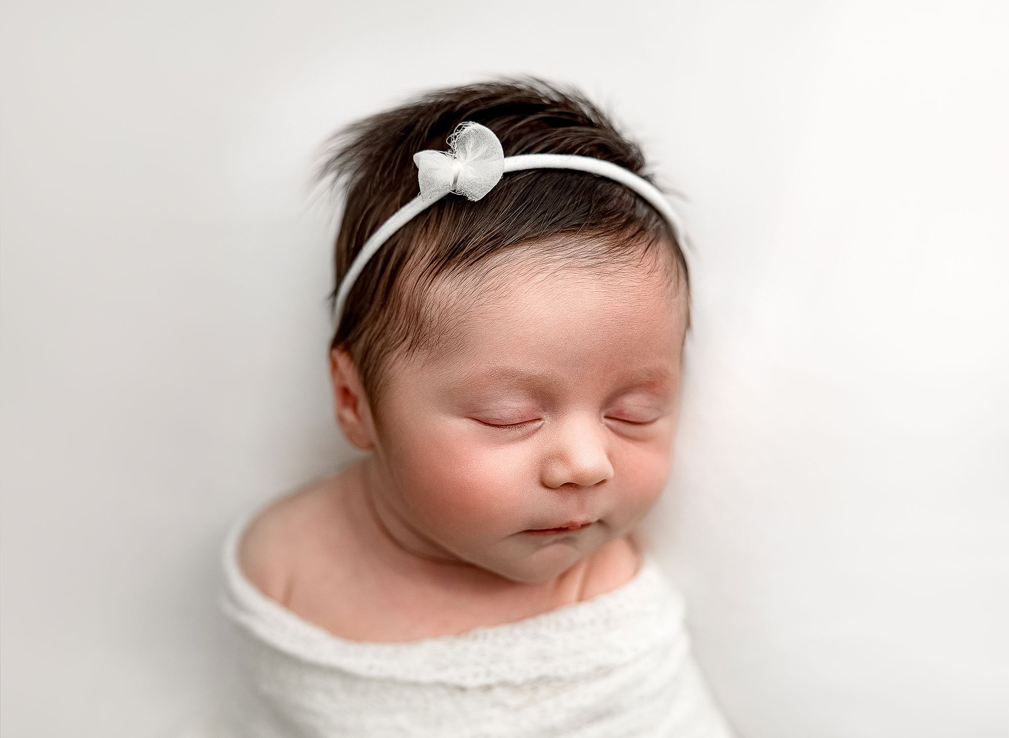Sleeping newborn baby with white headband and wrapped in a soft blanket.
