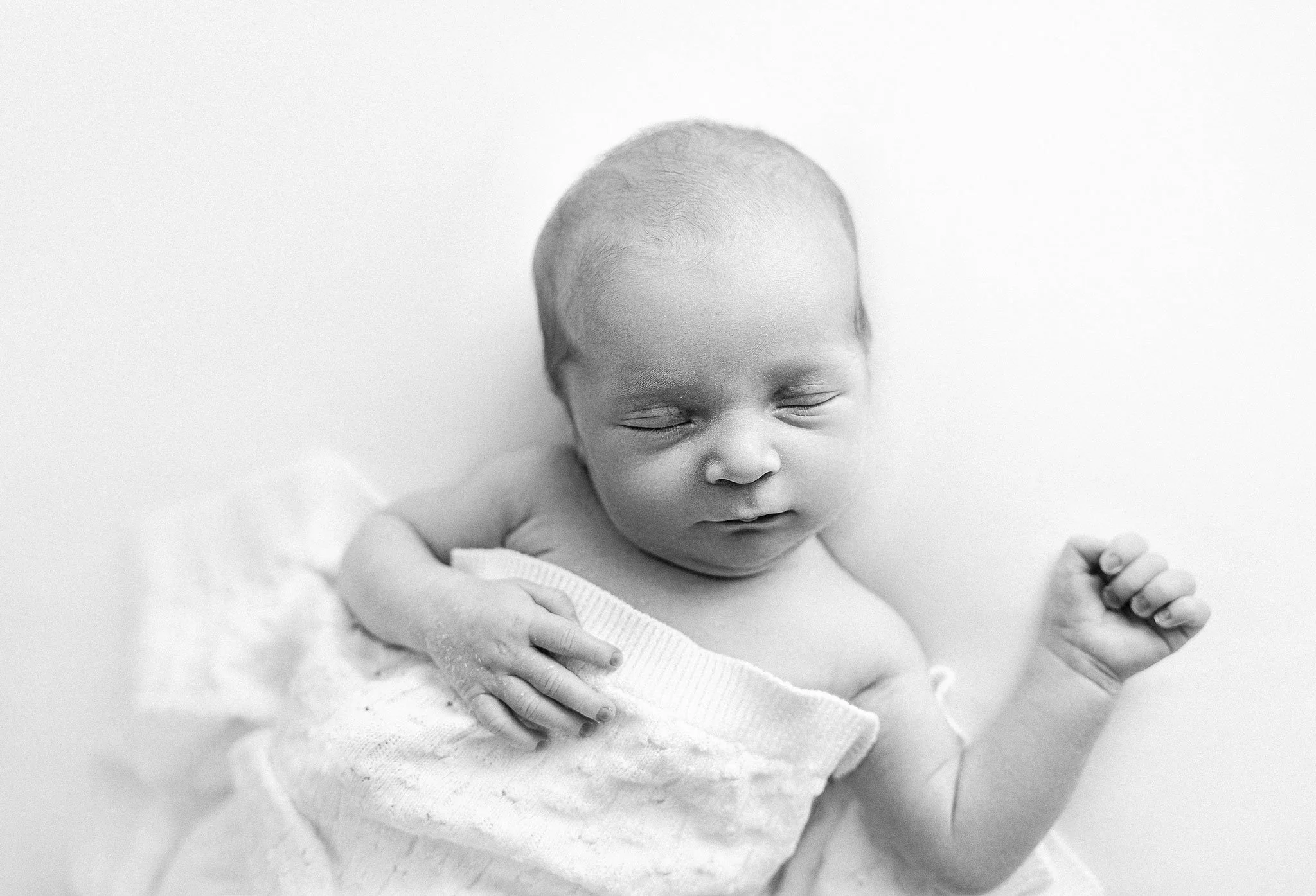 Black and white photo of a sleeping baby wrapped in a knitted blanket.