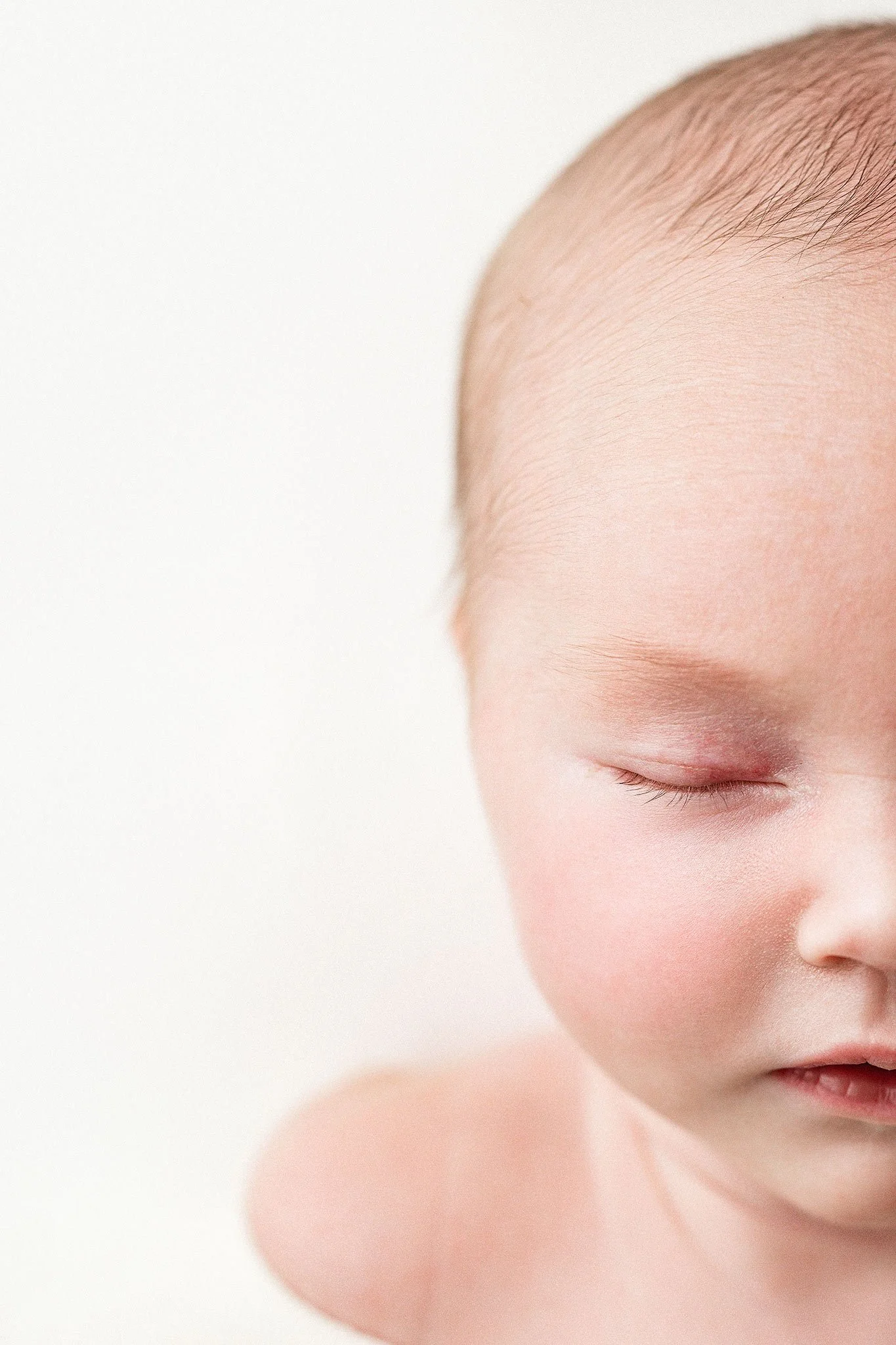 Close-up of a baby's face with closed eyes, smooth skin, and soft features against a plain white background.