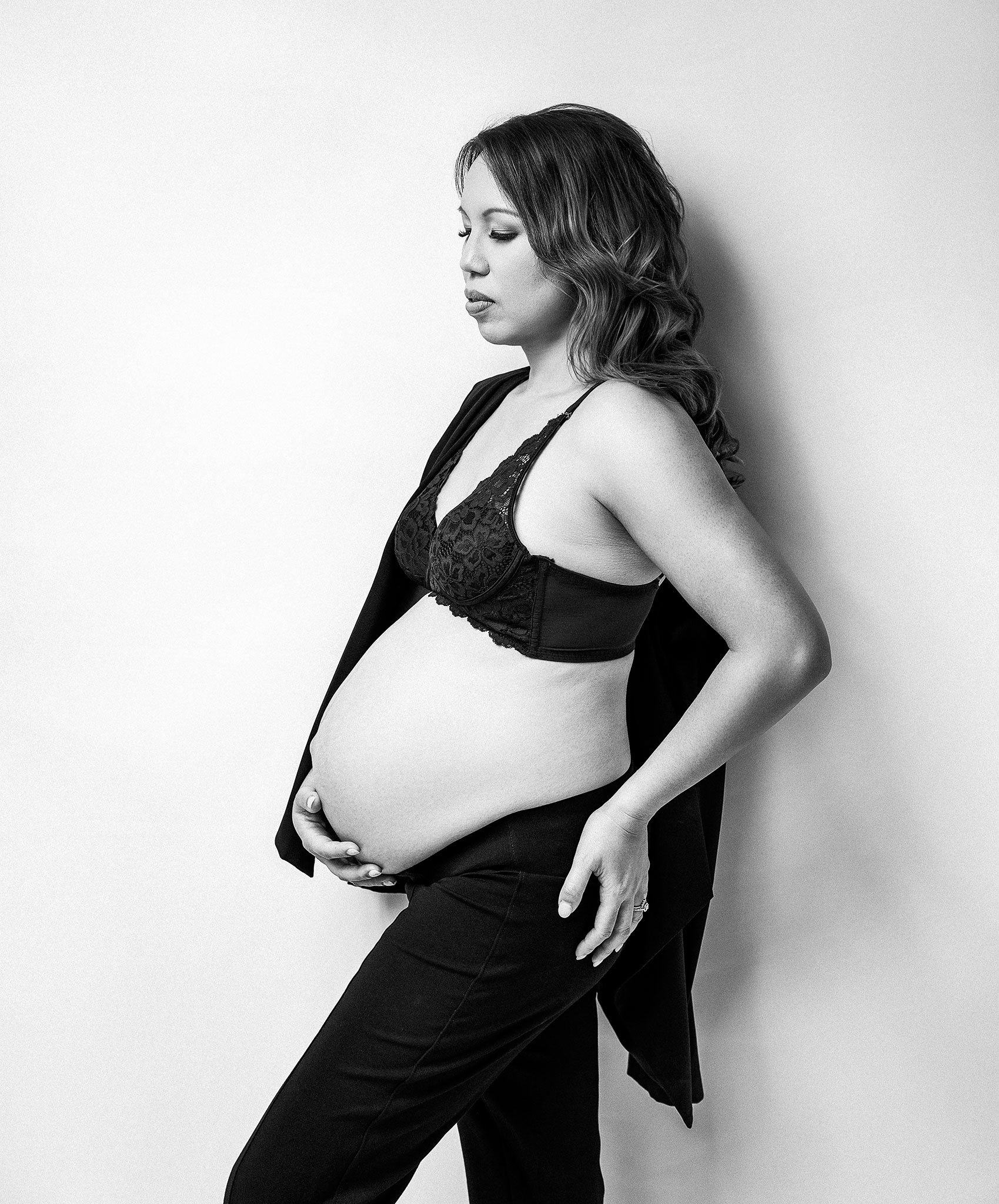 Pregnant woman in black lingerie and pants holding her belly in black and white.