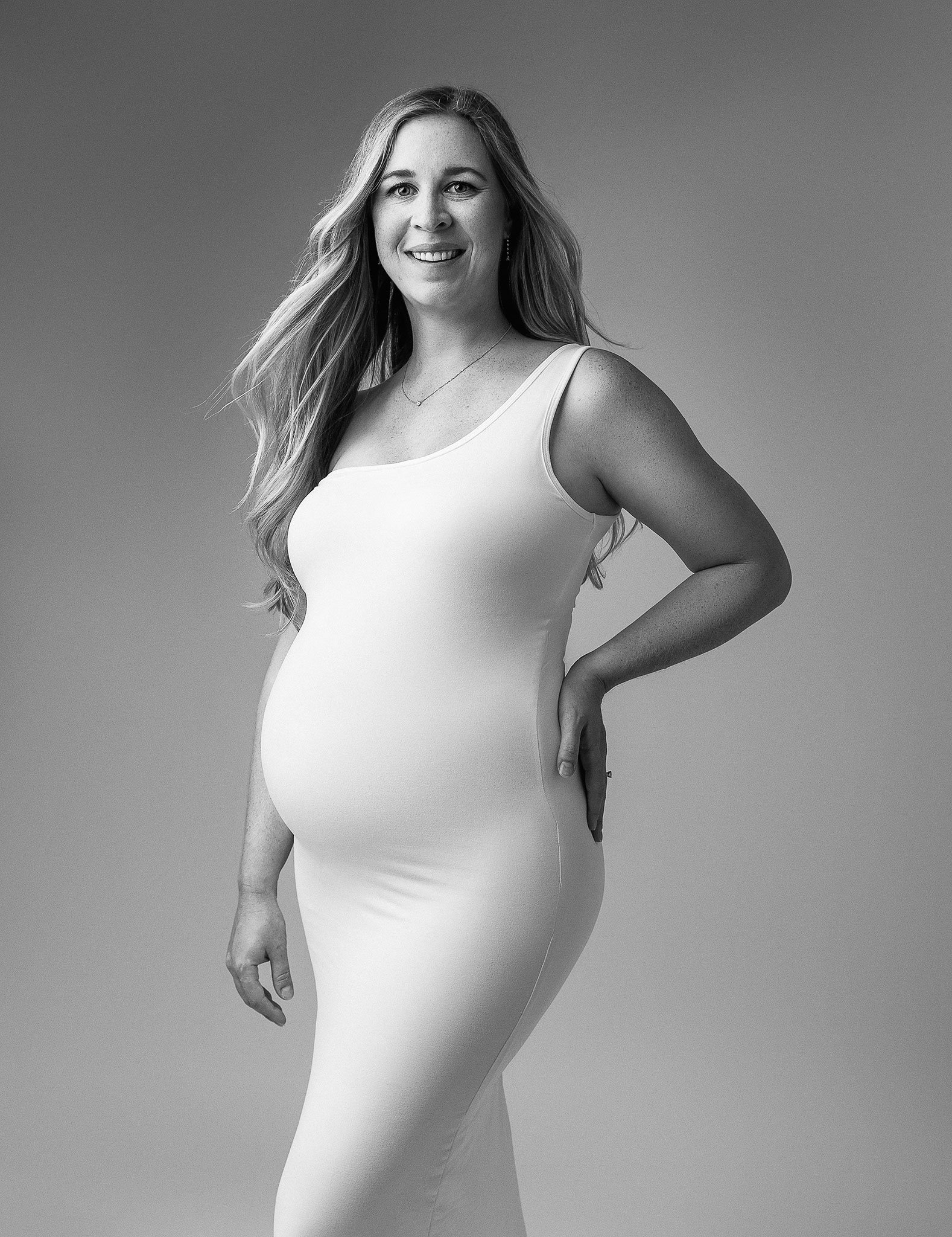 Pregnant woman in a white dress, posing in a studio setting.