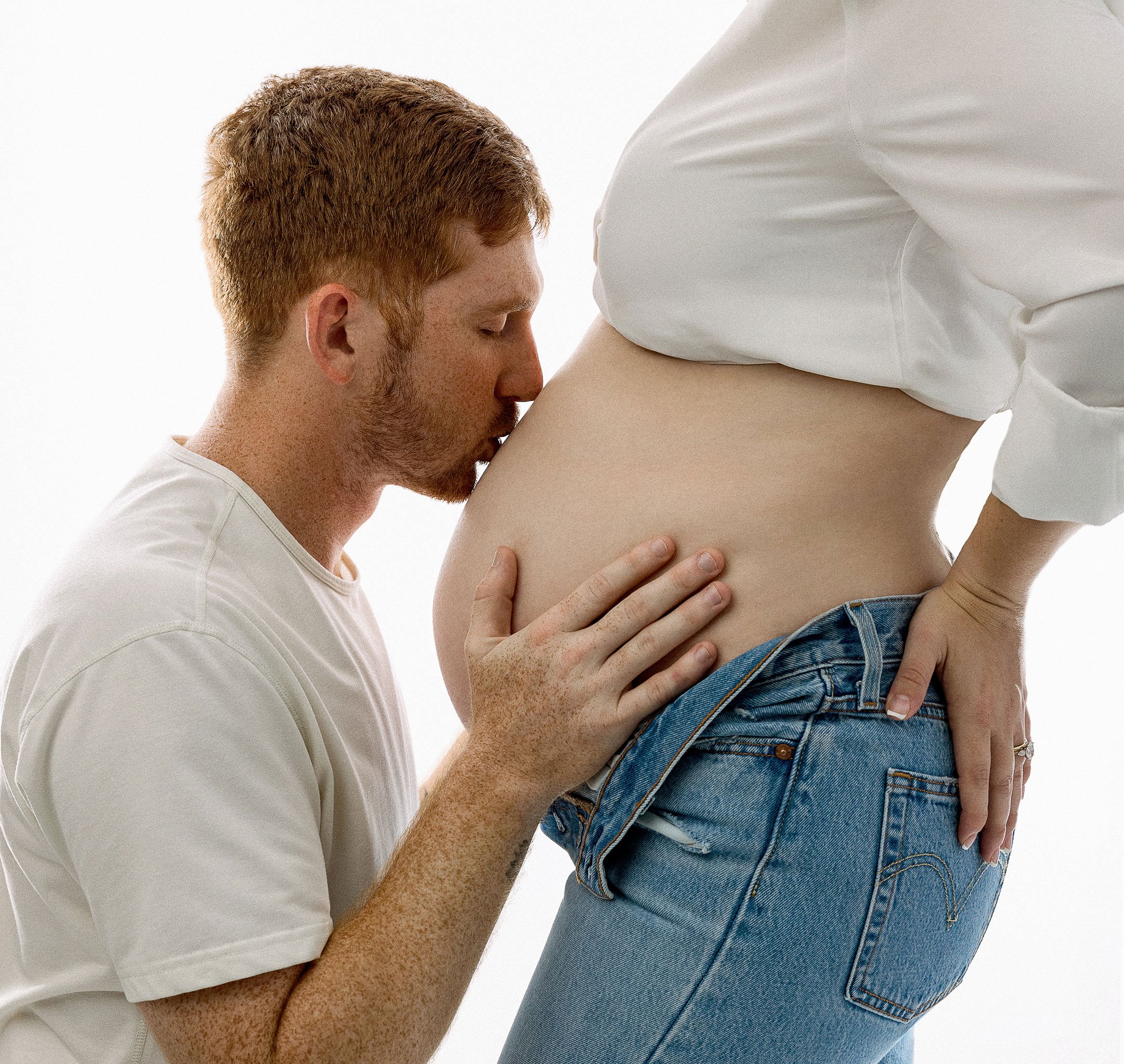 A man kissing a pregnant woman's belly, symbolizing love and anticipation.