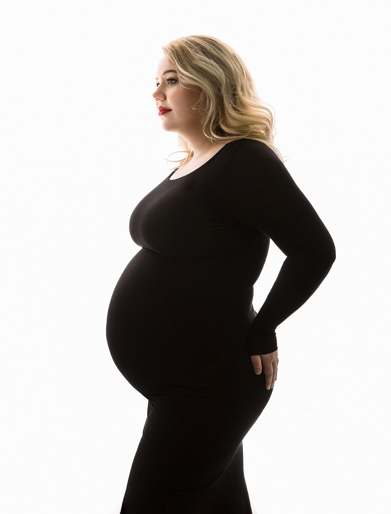 Pregnant woman in black dress, side profile, isolated on white background.