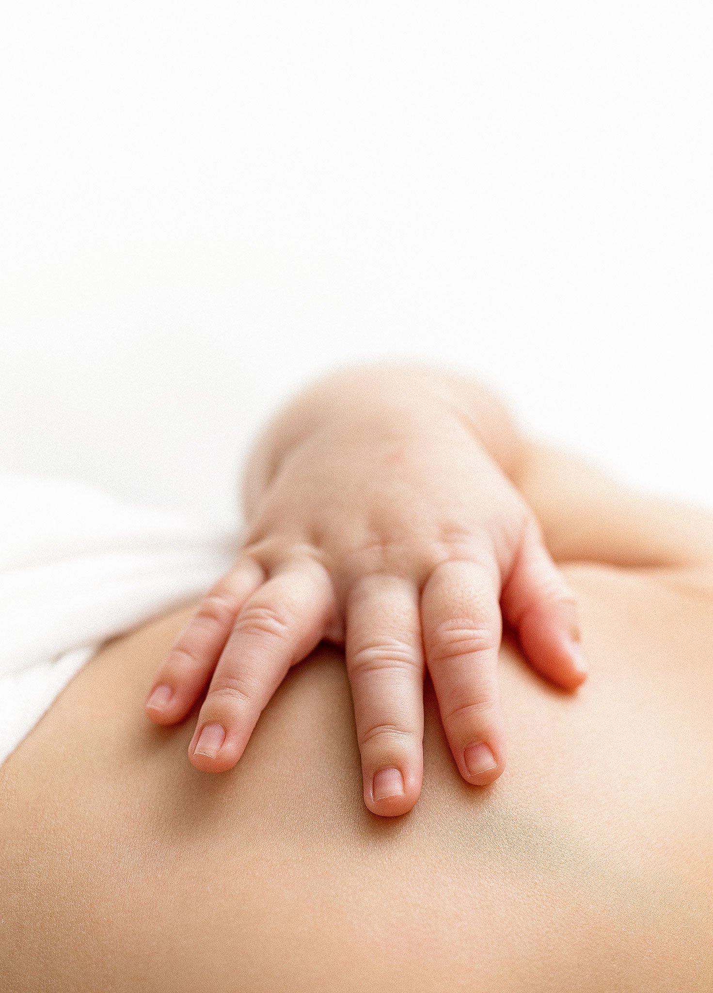 Close-up of a baby's hand gently placed on a person's back, resting on a white surface.