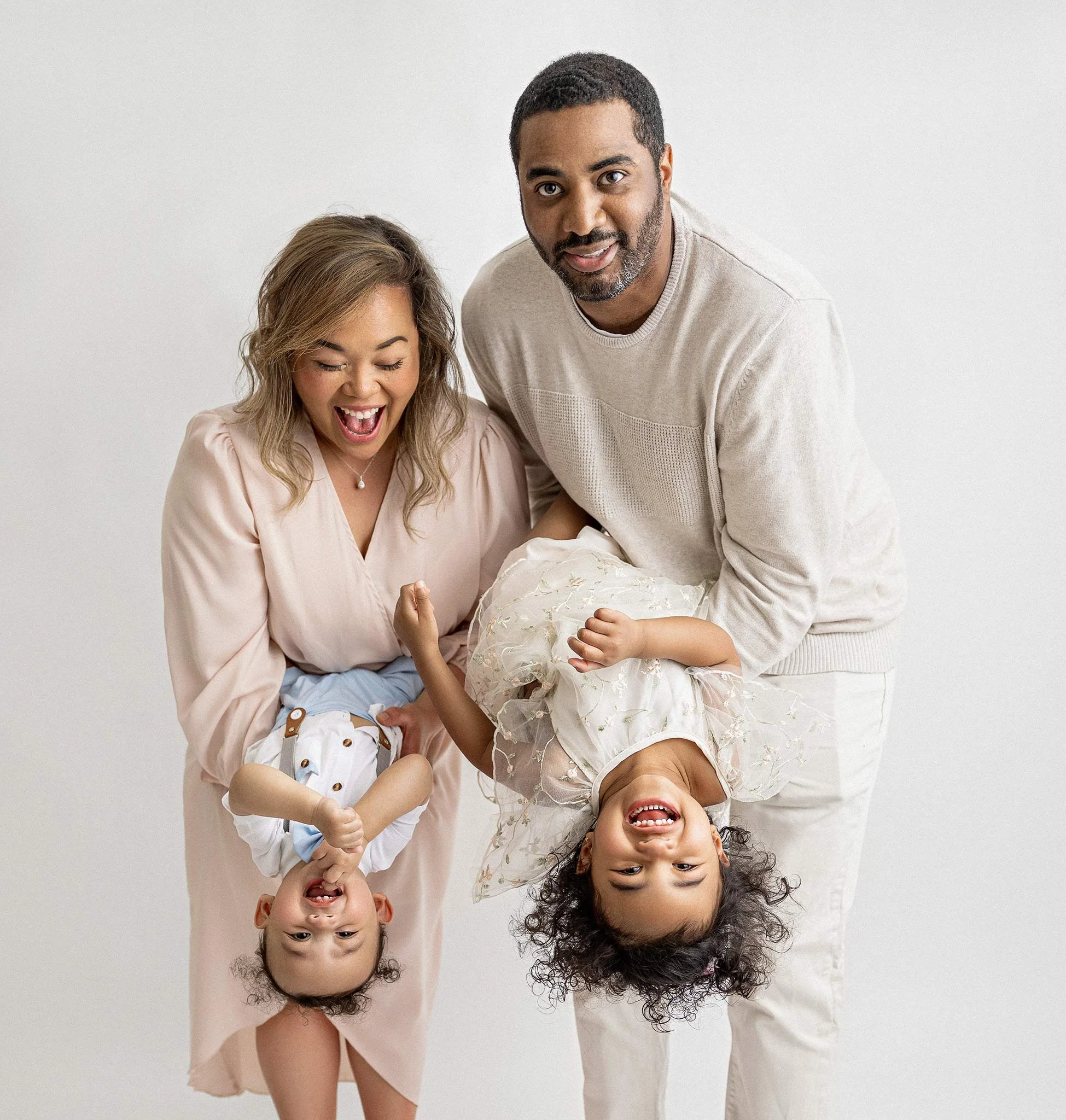 A cheerful family with parents holding their two young children upside down, smiling and playing.
