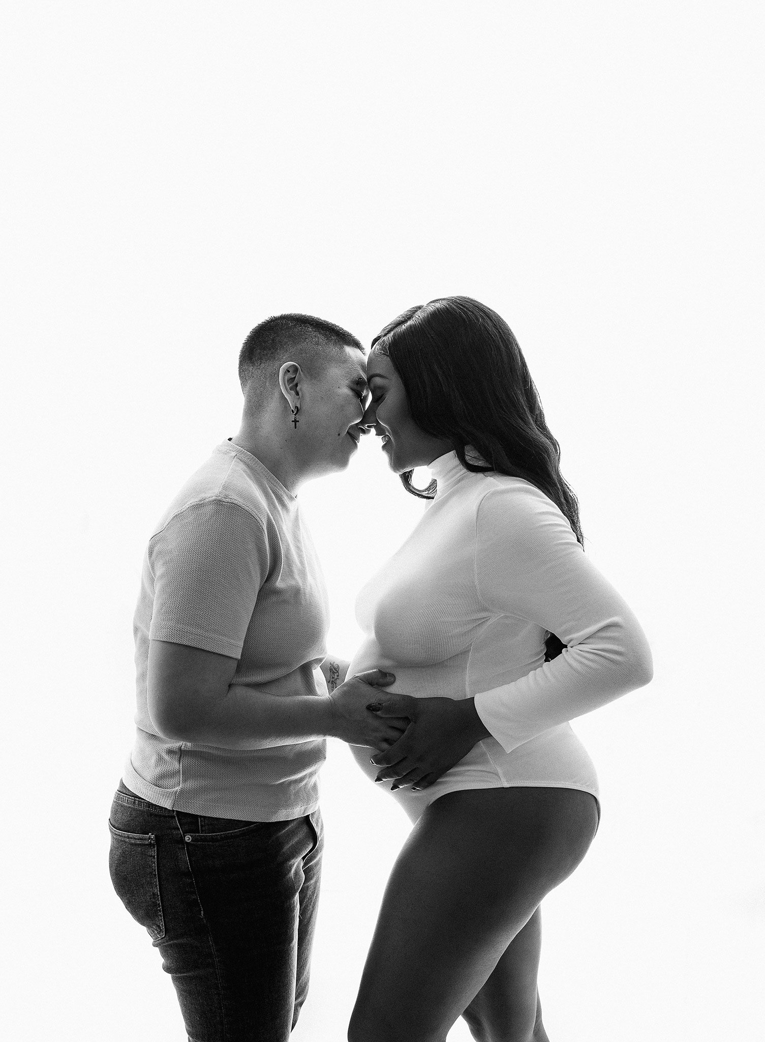 Pregnant woman and partner touching foreheads, smiling. Black and white photograph.
