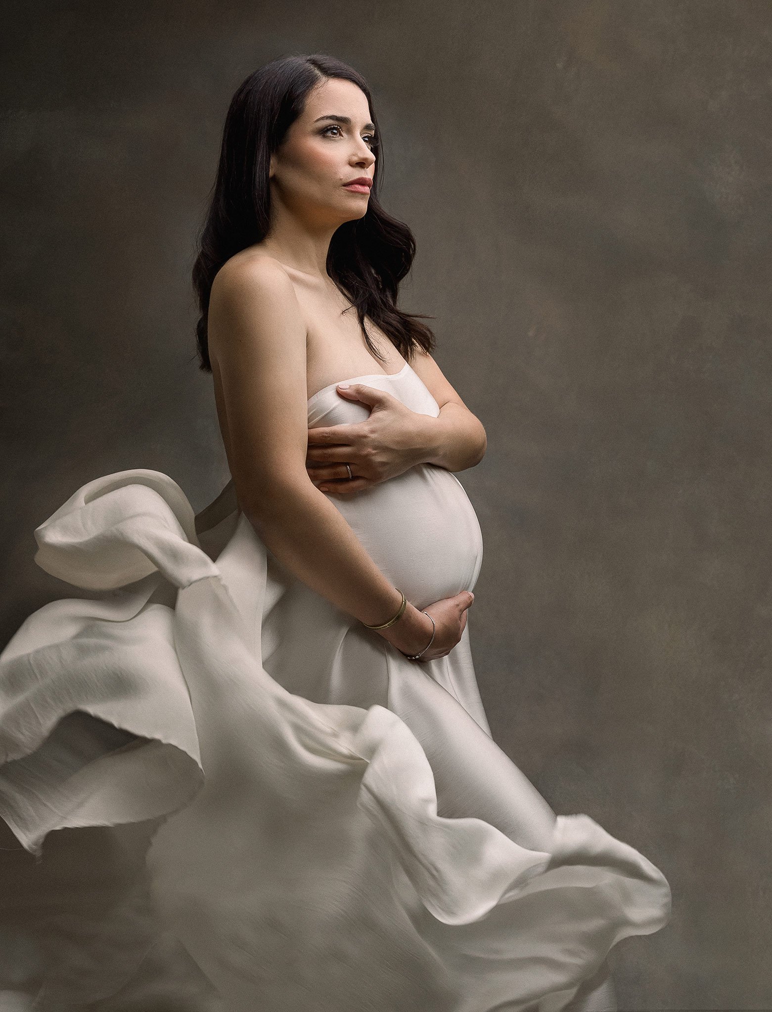 Pregnant woman in flowing white fabric, holding her belly.