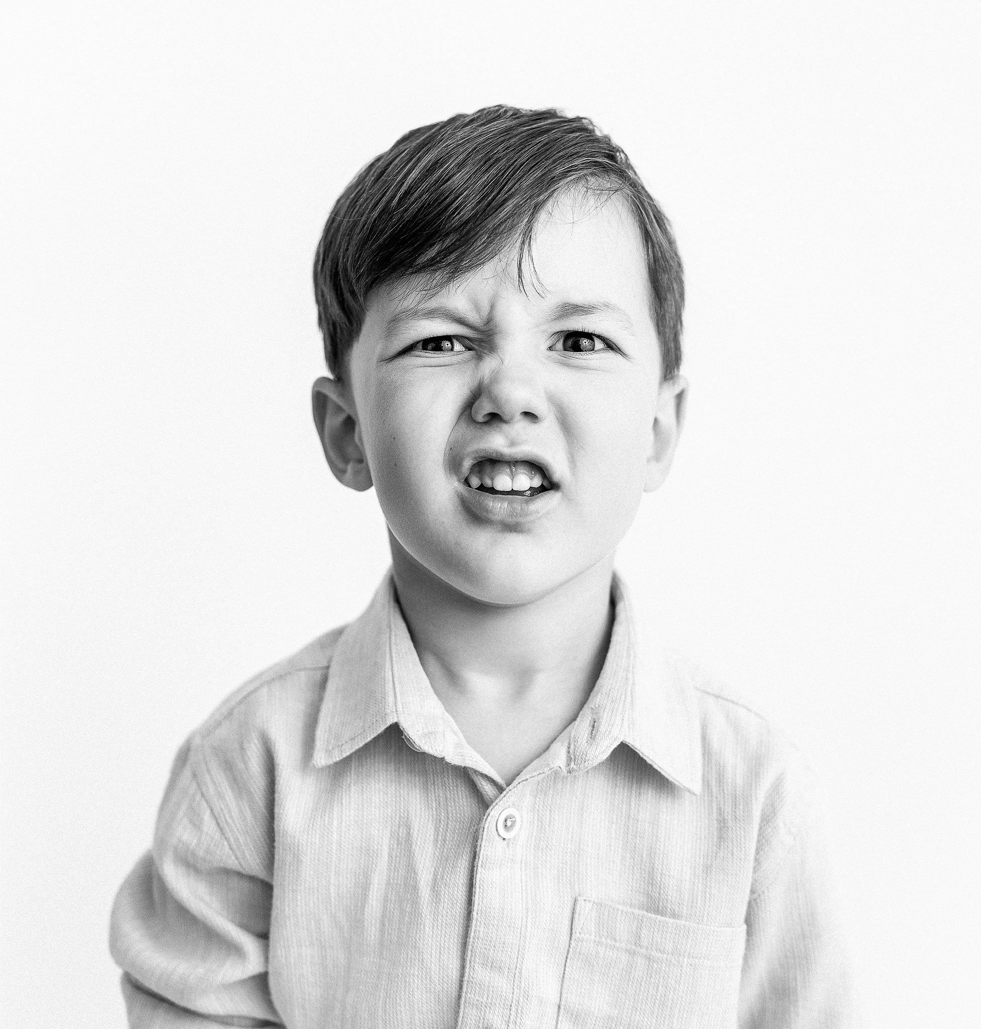 Black and white photo of a young boy making a funny expression, wearing a button-up shirt.