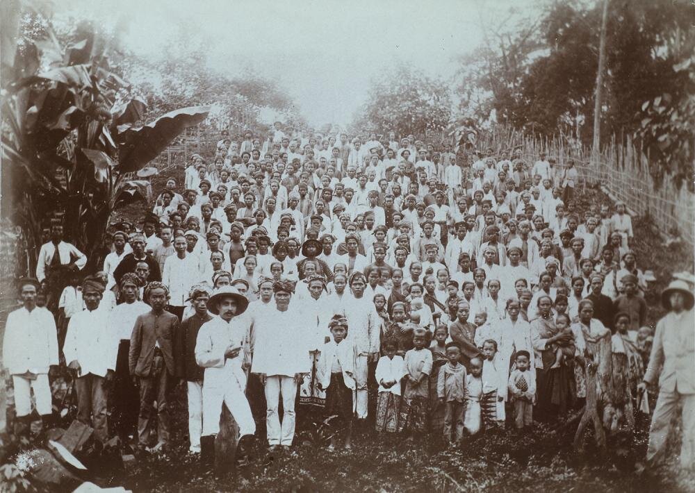  Hundreds of people by a hill and three overseers. Group portrait of laborers at the Way Lima farming business, Lampong Districts | TM-60013351 