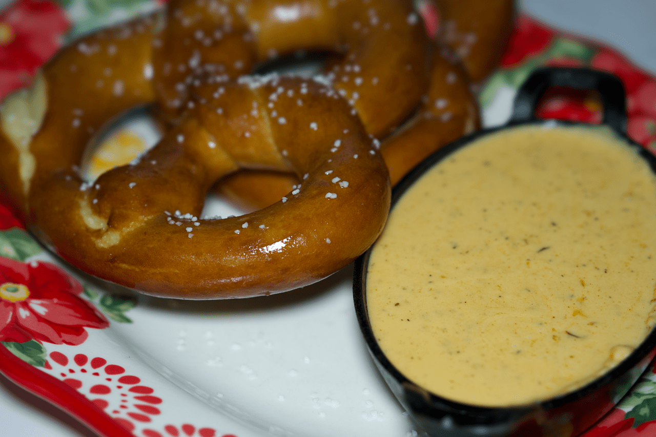 Close-up of a glazed pretzel sprinkled with coarse salt on a Christmas-themed plate with a small dish of mustard nearby.