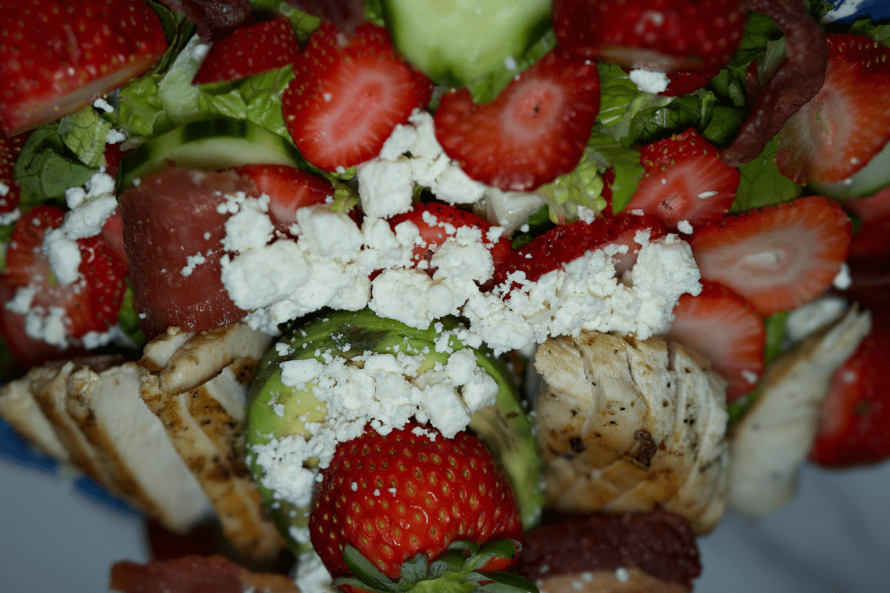 Close-up of a strawberry and grilled chicken salad with crumbled white cheese and chopped greens.